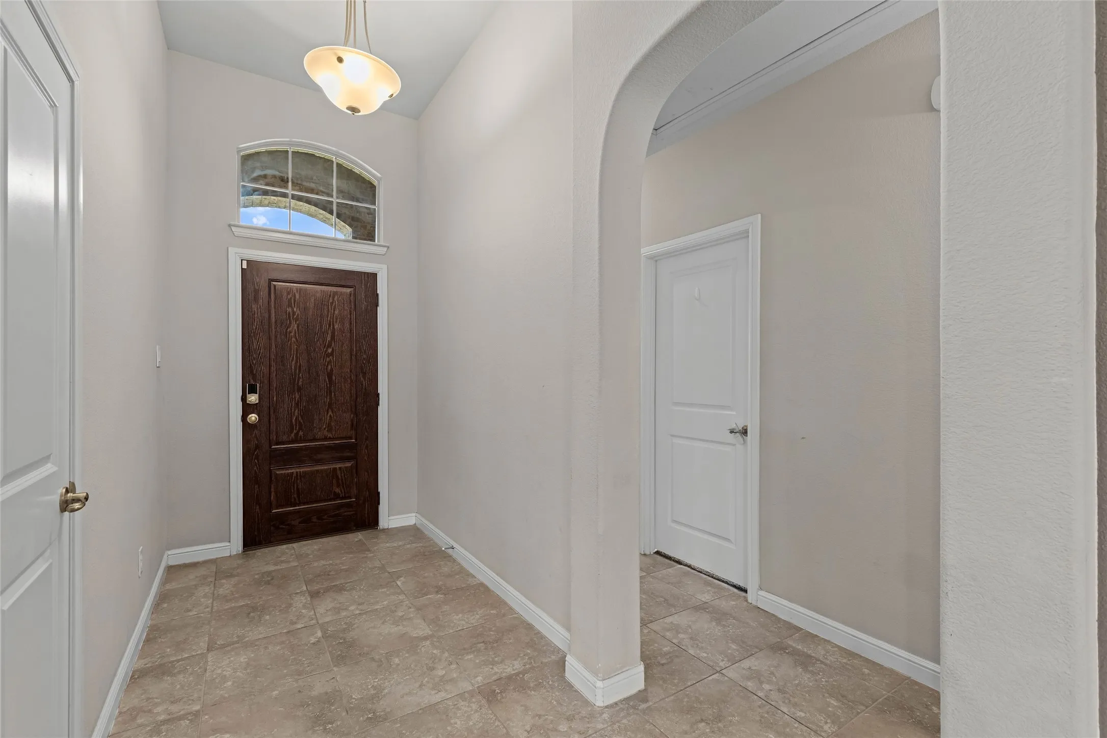 Arched entryway with a dark wood-finish entry door, transom window, and tile flooring