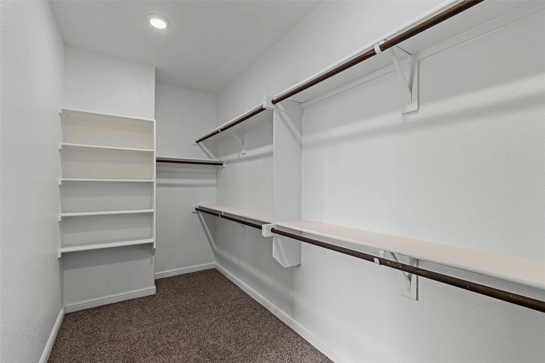 Walk-in closet with integrated shelving, multiple hanging rods, and recessed lighting