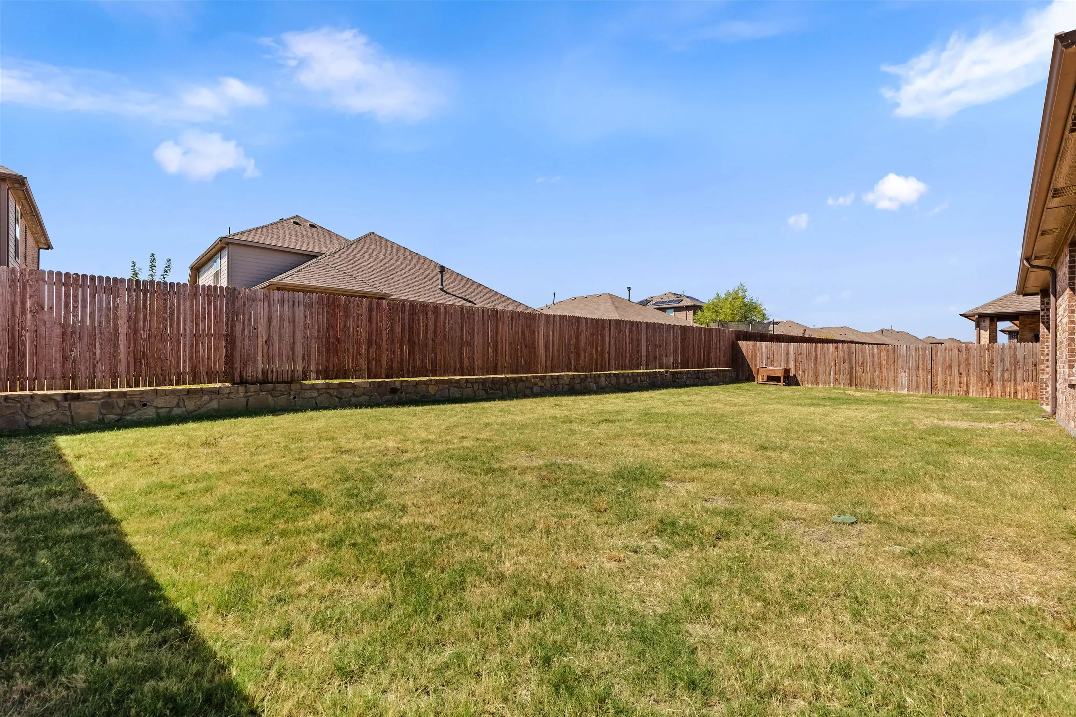 Expansive backyard with a level lawn, full wood privacy fencing, and a decorative stone retaining wall