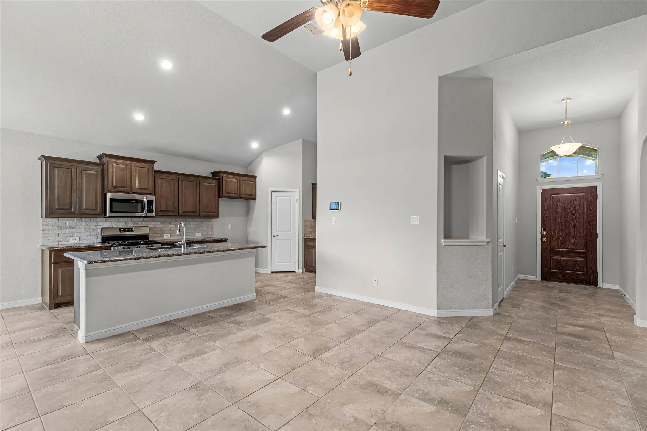 Vaulted ceilings with recessed lighting, tile flooring, kitchen island with granite countertop, dark wood cabinetry, and stainless steel appliances