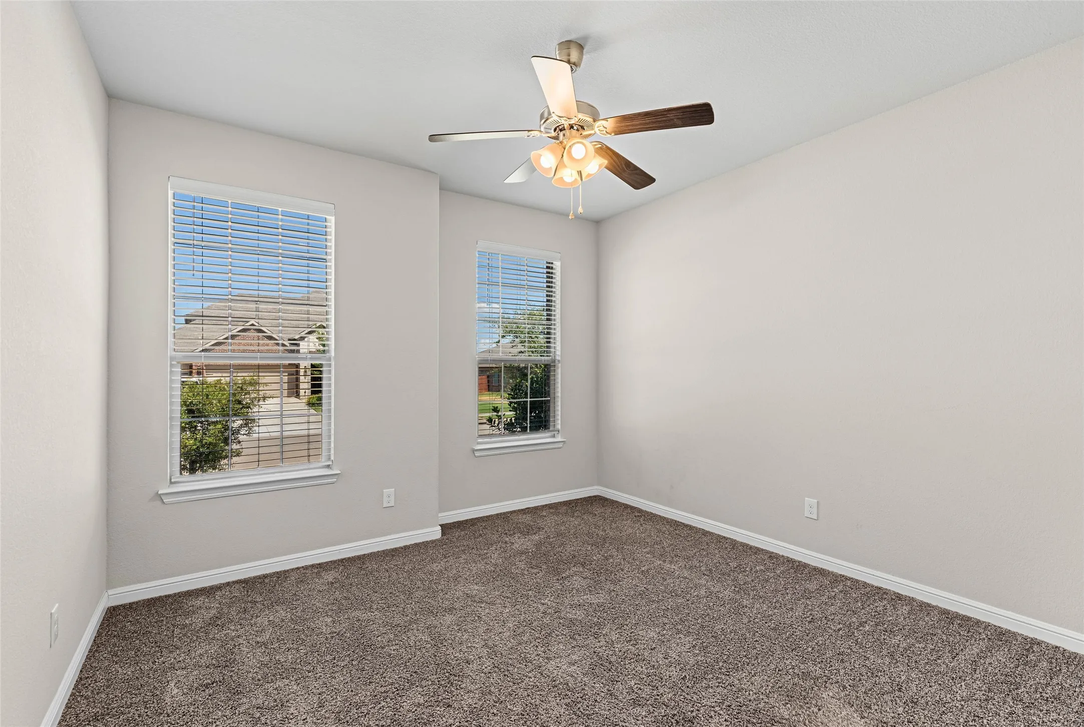Neutral tone wall paint, dual windows with blinds, ceiling fan with integrated lighting, and textured carpeting