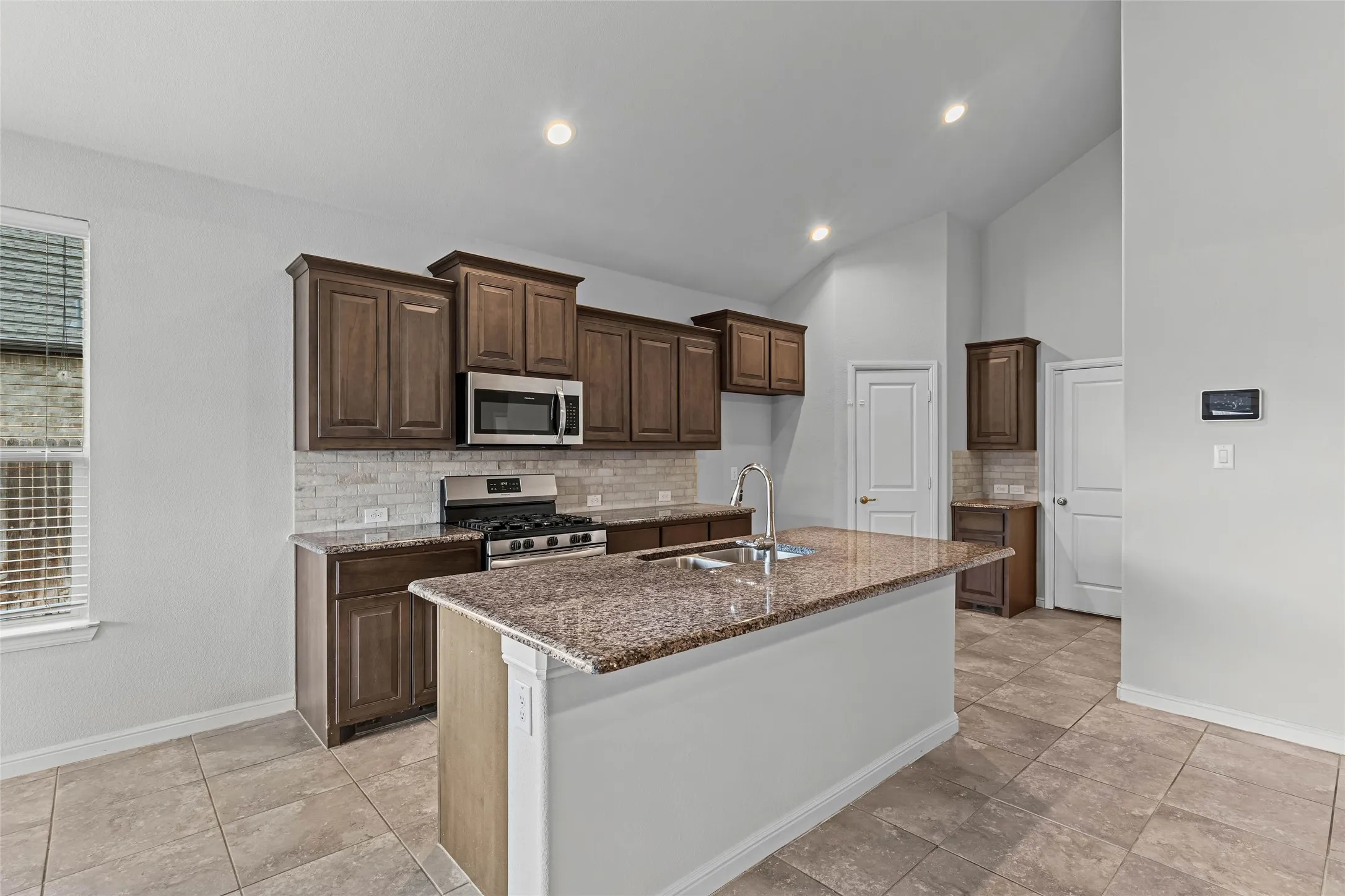 Kitchen featuring a center island with sink, stainless steel appliances, dark wood cabinetry, tile flooring, and recessed lighting