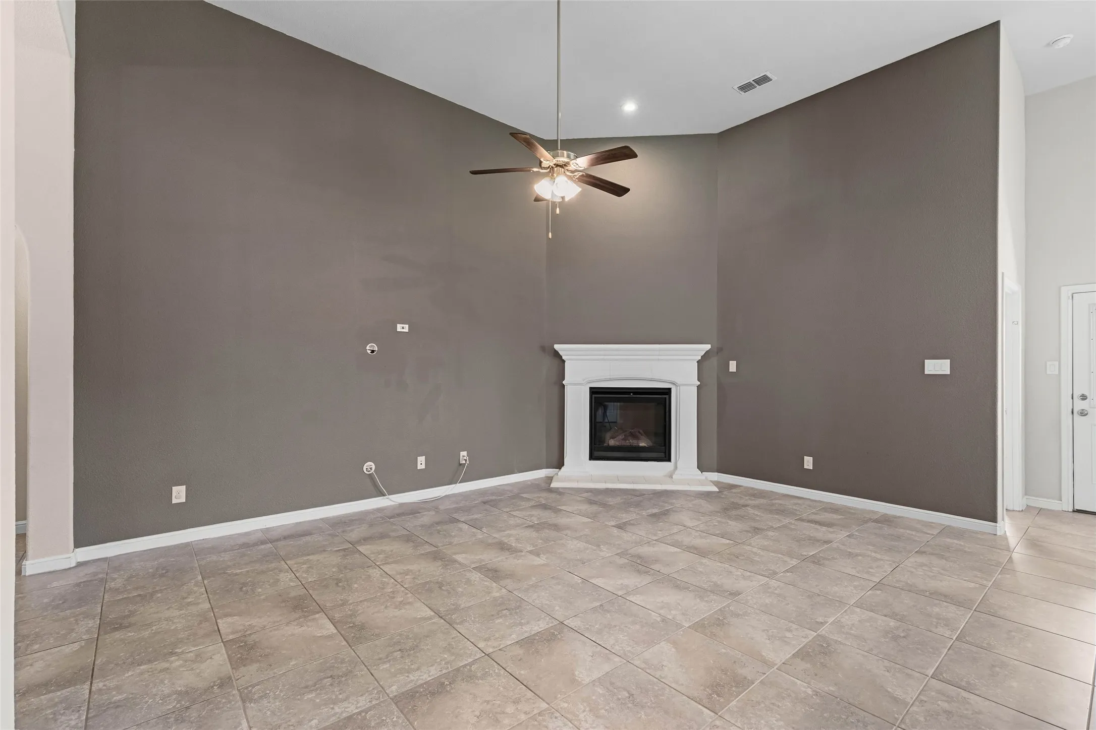 Vaulted ceiling, ceiling fan, recessed lighting, corner fireplace with mantel, and tile flooring