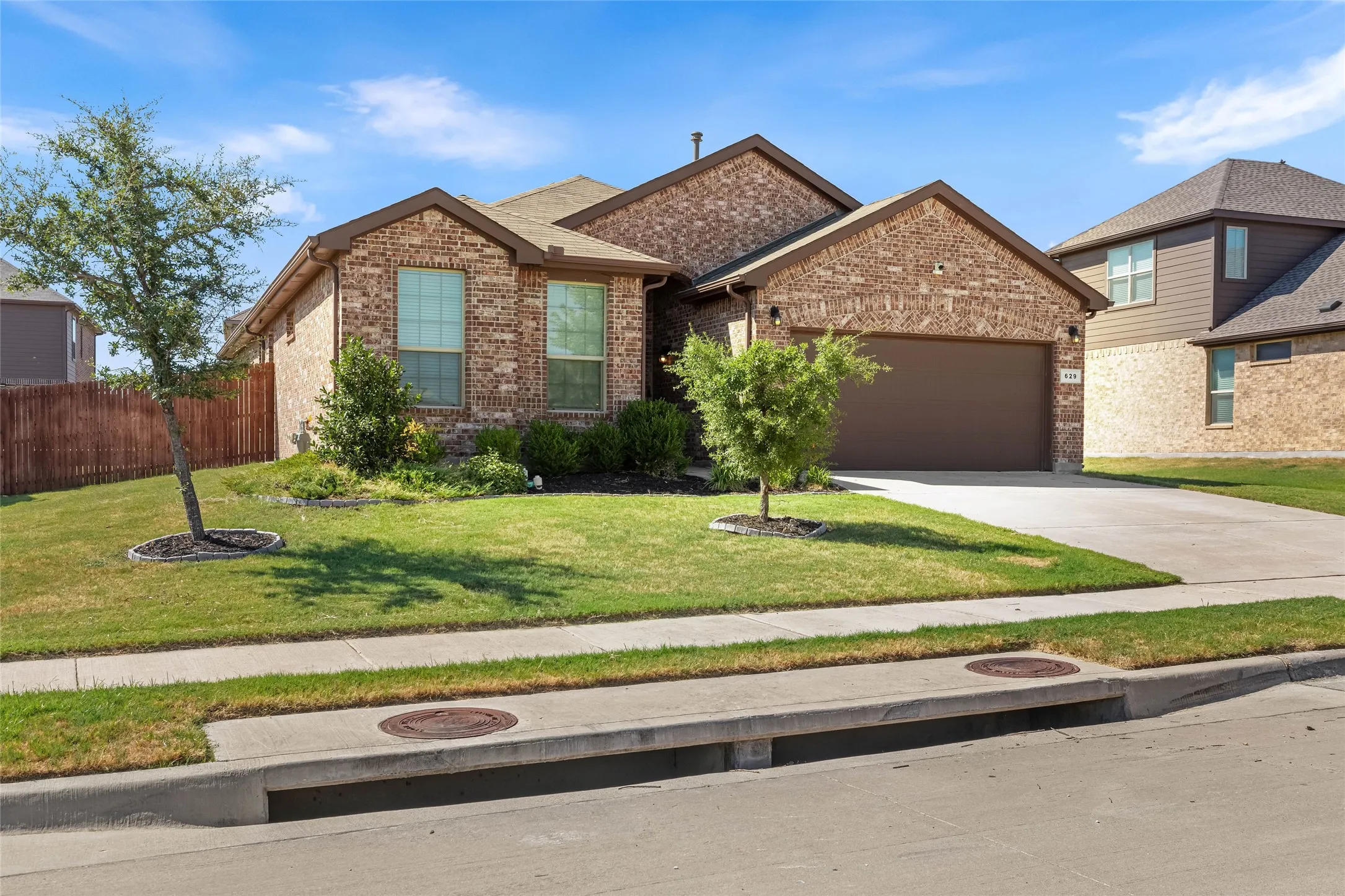 Brick exterior, attached garage, concrete driveway, front lawn, and established landscaping
