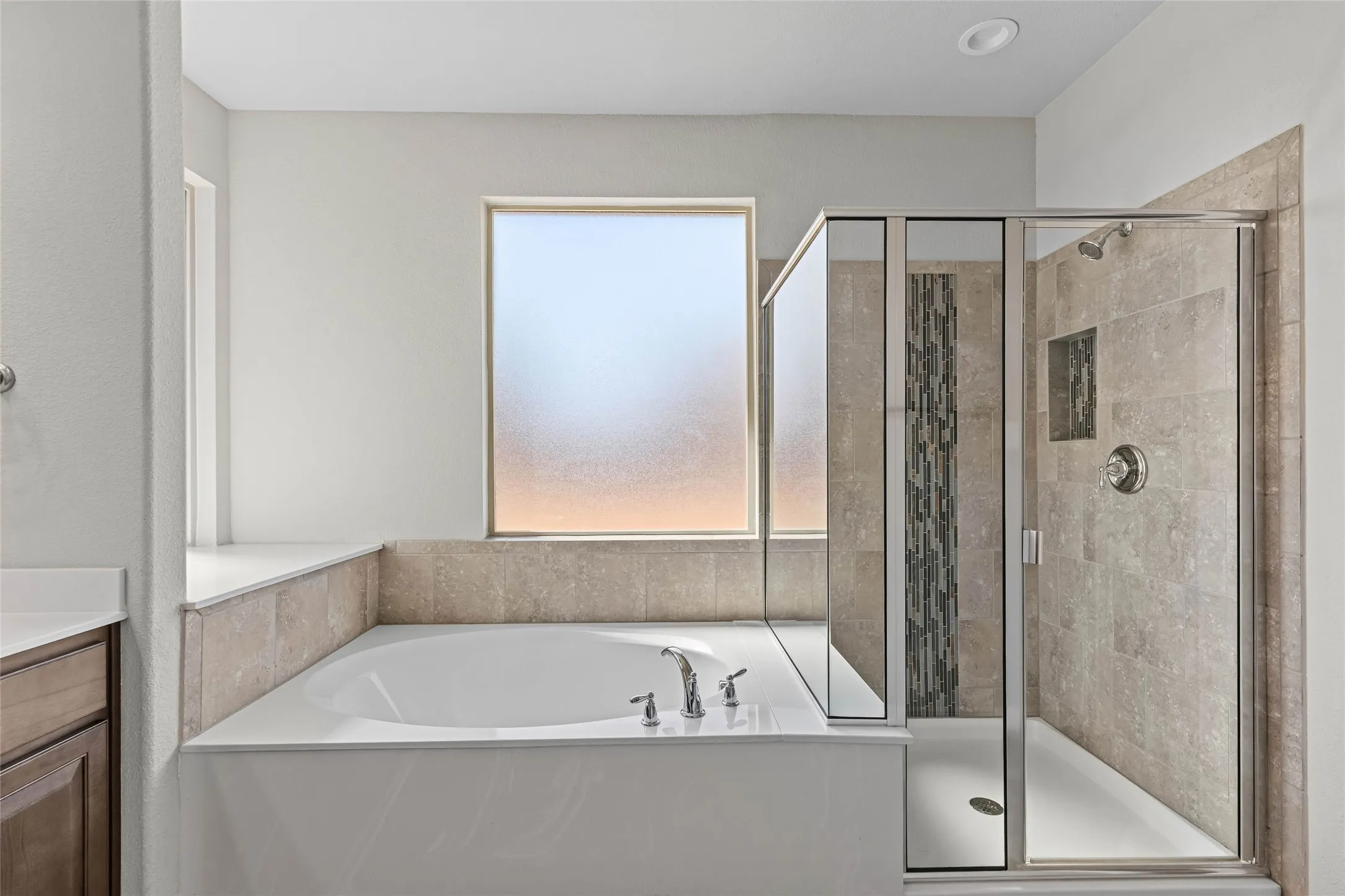 Built-in soaking tub with deck-mounted fixtures, glass-enclosed shower, tiled shower surround with accent mosaic, recessed shower niche, and frosted window