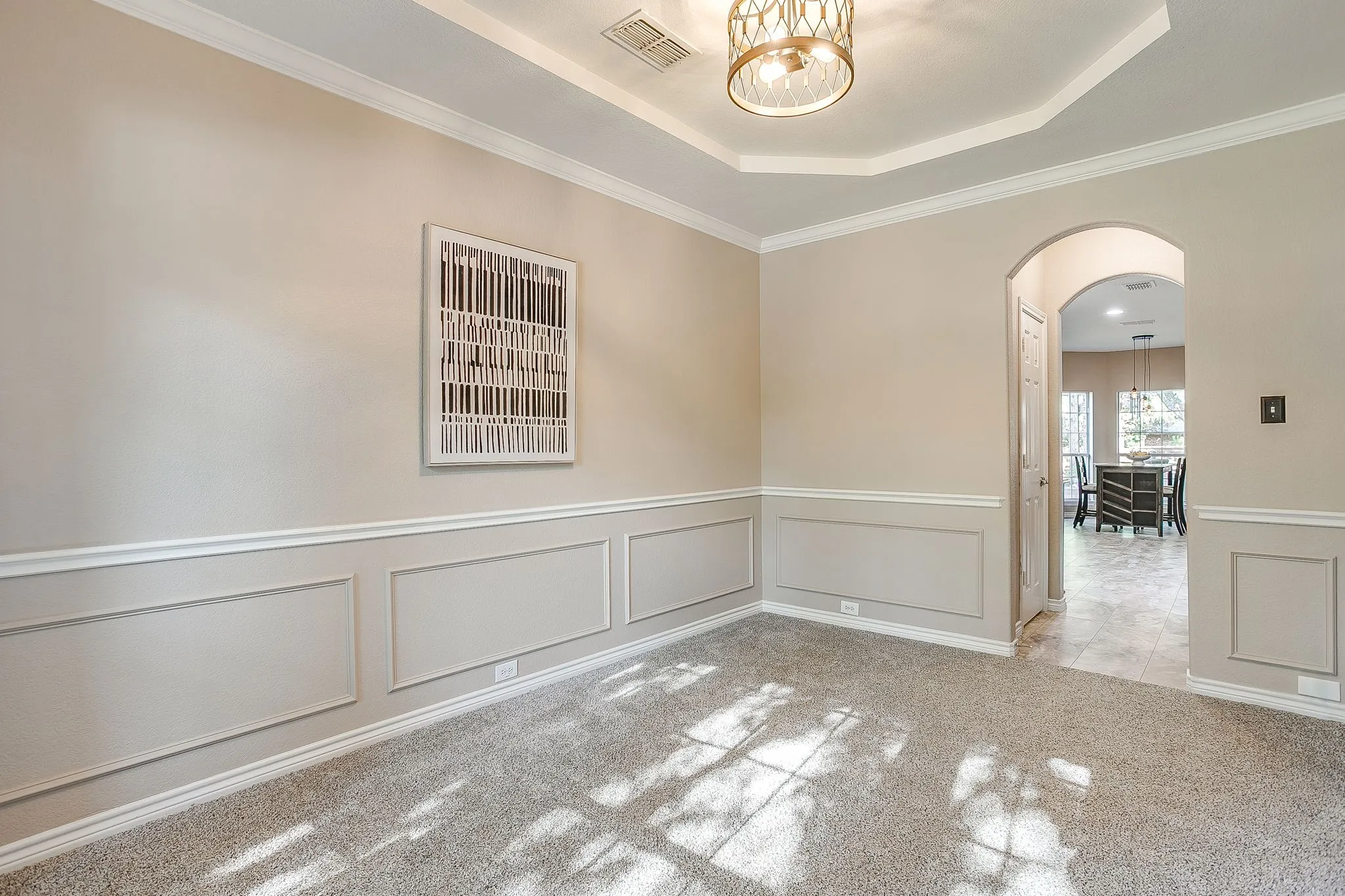 Wainscoting and crown molding details, tray ceiling, recessed lighting, and an arched doorway