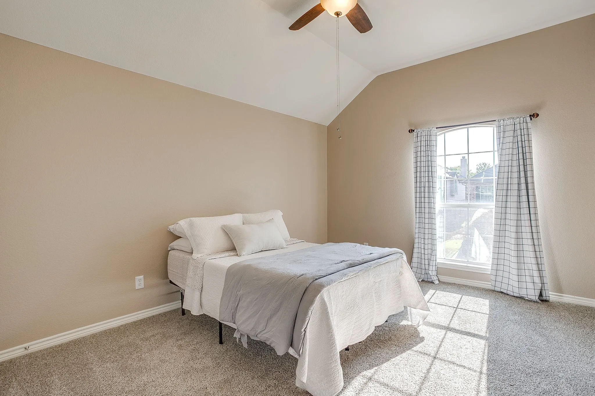 Vaulted ceiling with an attached ceiling fan, neutral paint, light-colored carpet, and a large window