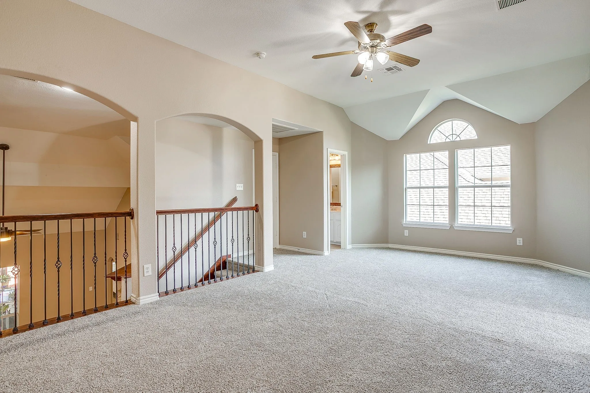 Open loft area featuring vaulted ceilings, arched doorways, a ceiling fan with light, and multiple windows including an arched transom