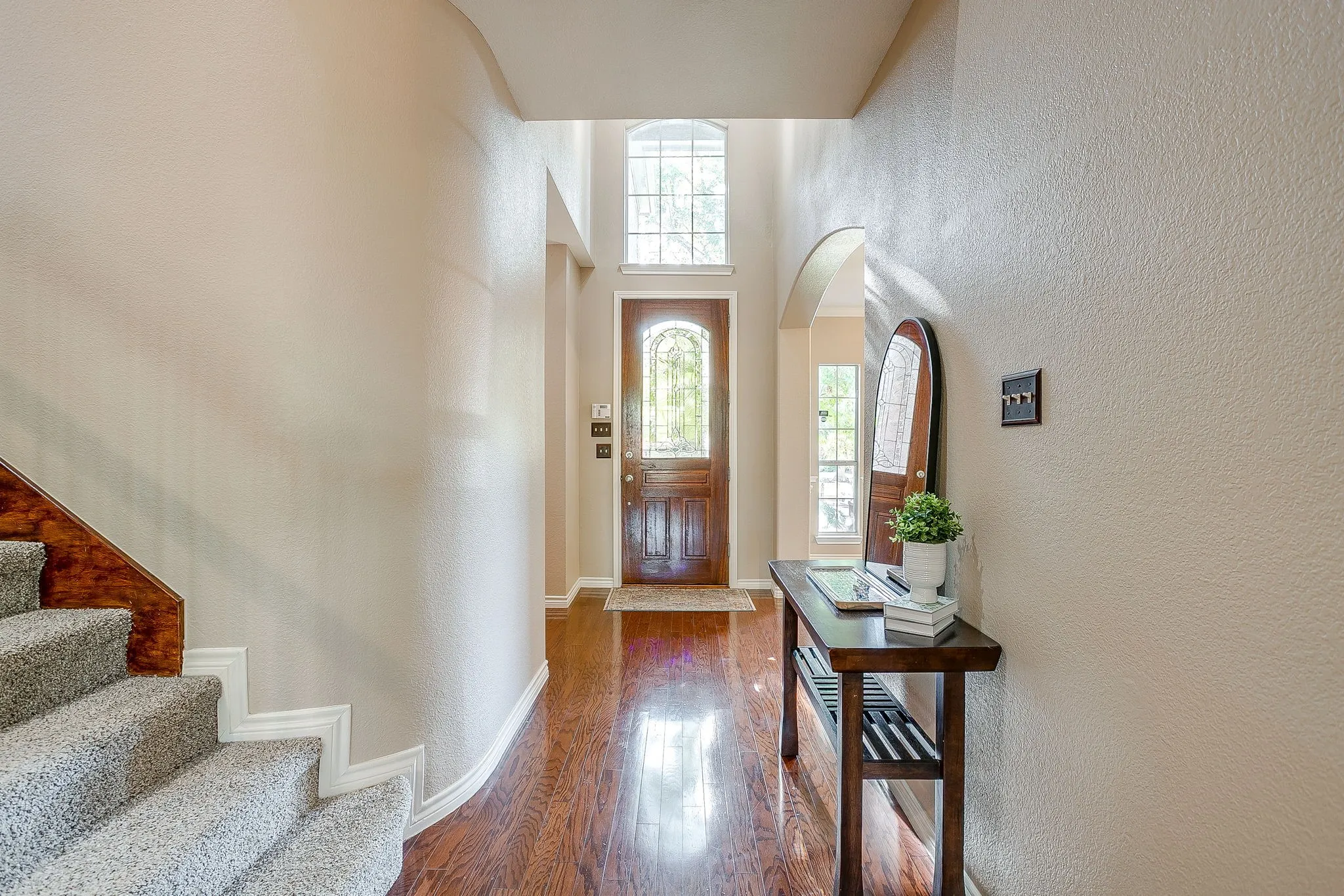 Wood-finish flooring, arched entryway, a detailed wood entry door, and a carpeted staircase with wood railing