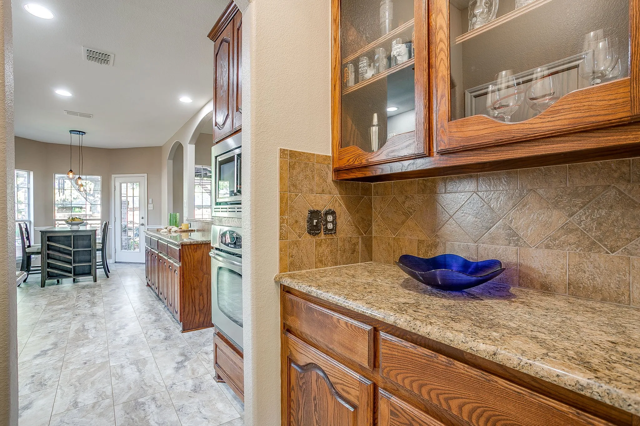 Full-height wood cabinetry with glass door accents, tiled backsplash, light-toned countertops, built-in stainless steel appliances, and recessed lighting