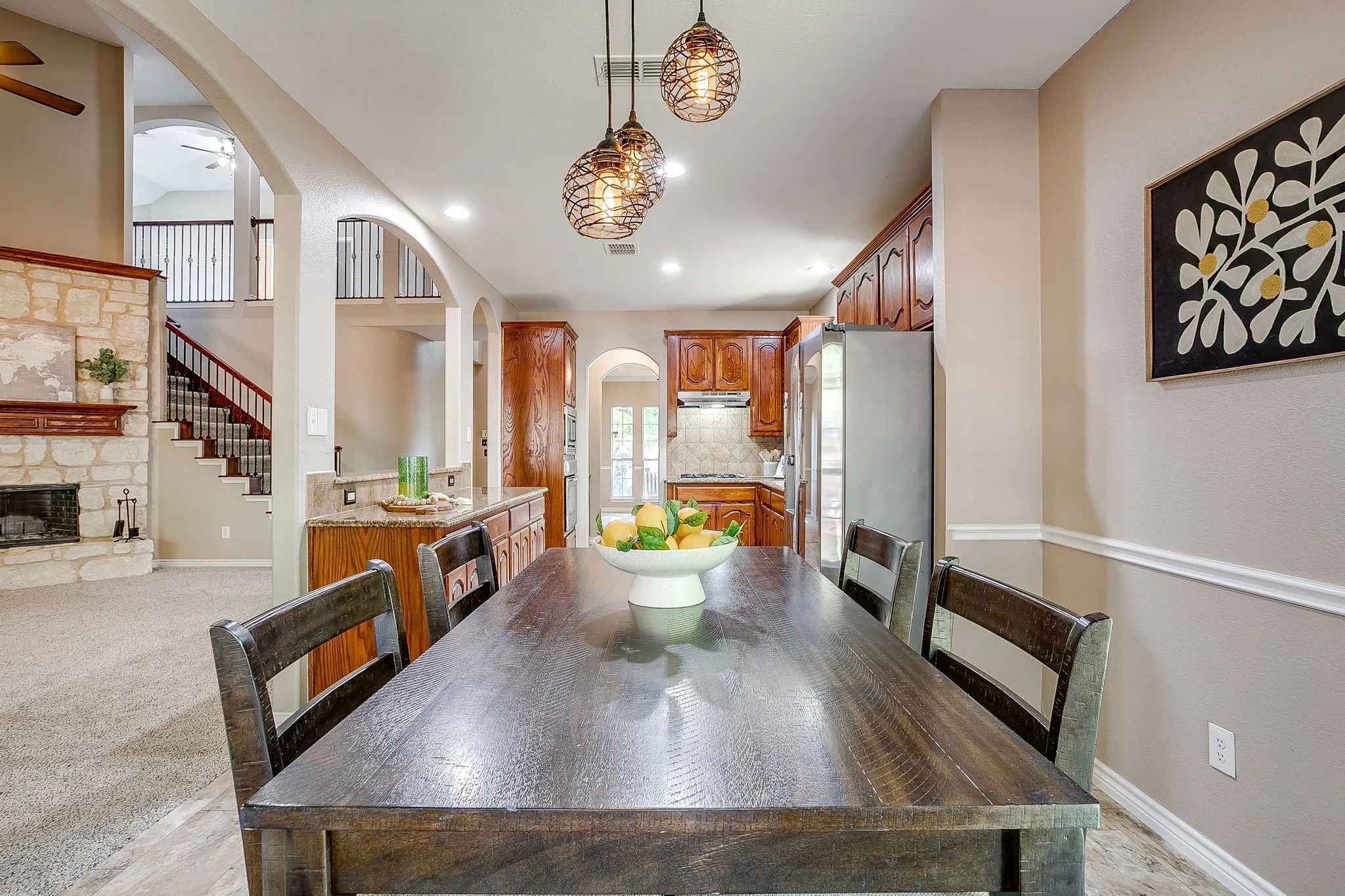 Open-concept design featuring a stone fireplace, wood staircase with dark iron balusters, and arched doorways