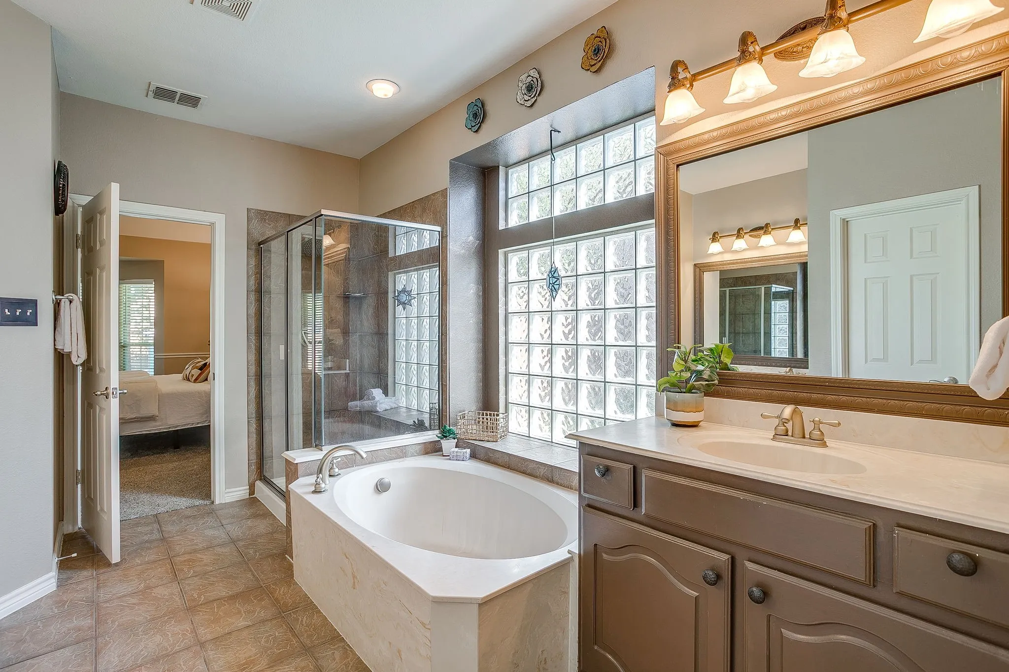 Built-in soaking tub, glass block window, glass-enclosed shower, single vanity with integrated sink, and tile flooring