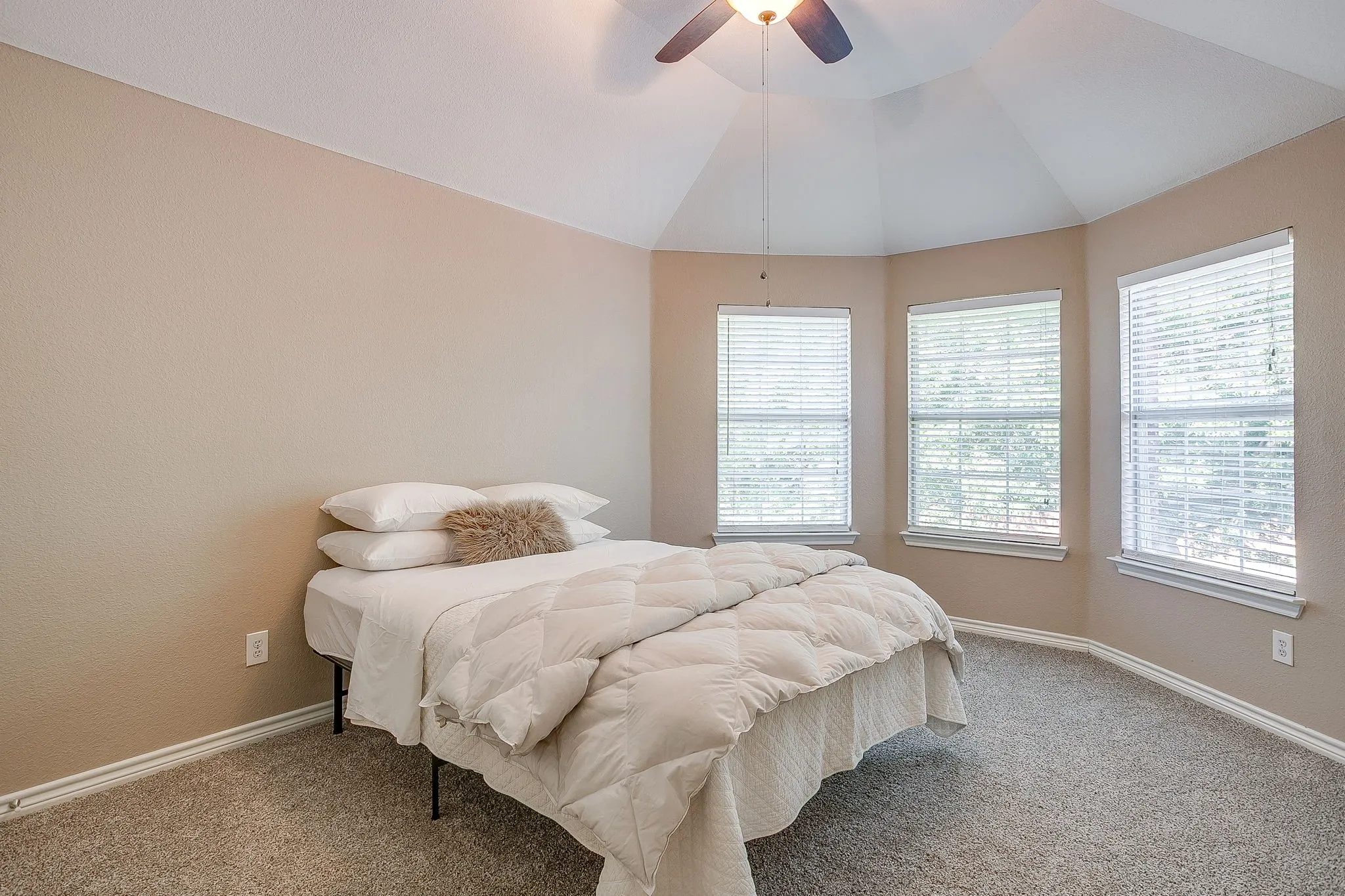 Vaulted ceiling, carpeted flooring, three windows with blinds, and a ceiling fan