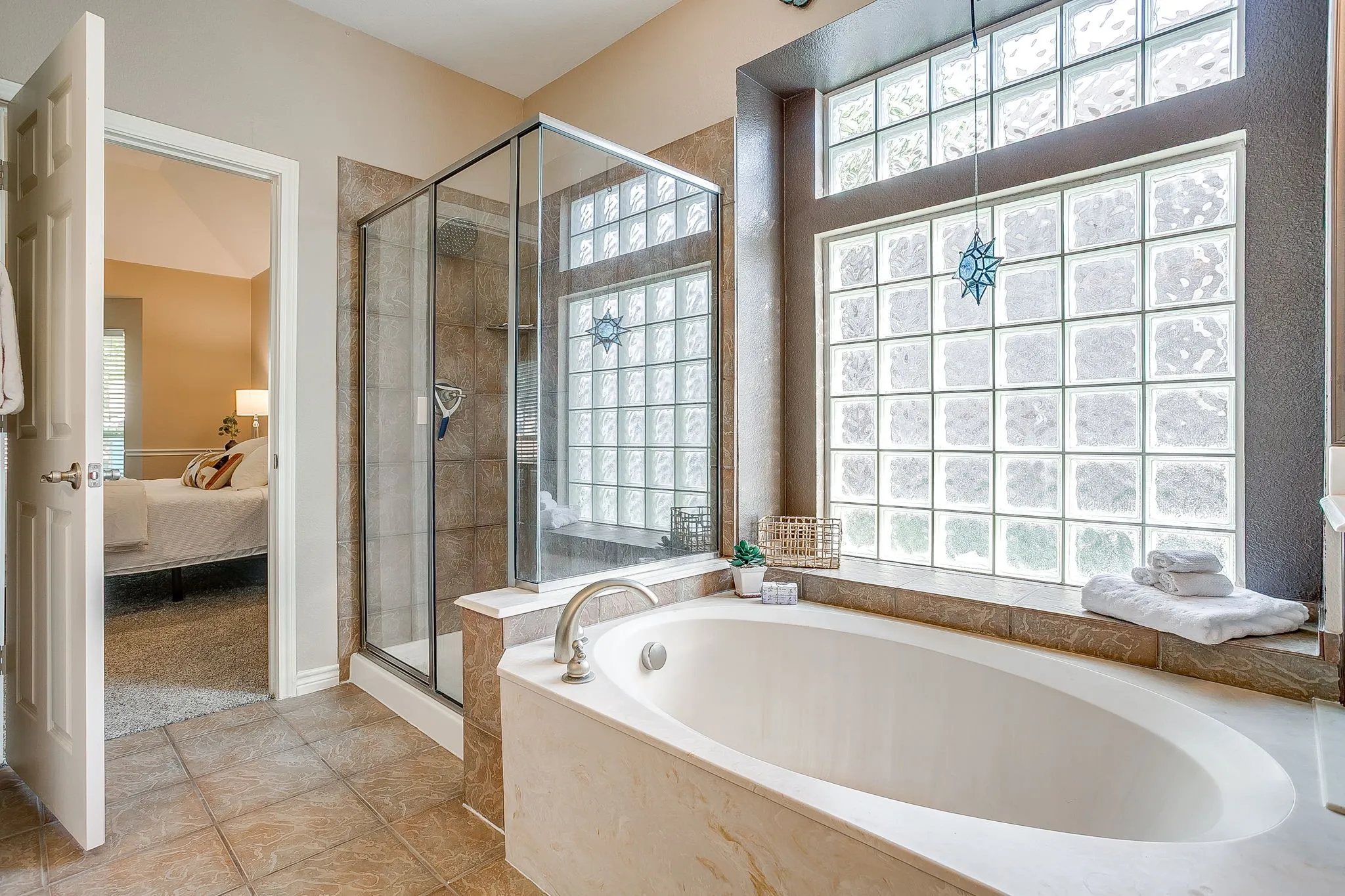 Soaking tub with deck-mounted fixtures, glass block window, and a tiled walk-in shower with a built-in bench