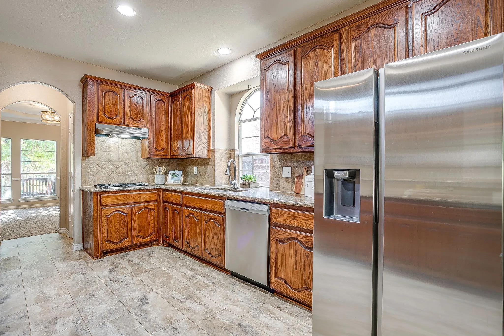 Kitchen featuring wood cabinetry, stainless steel appliances, a tile backsplash, and a large arched window