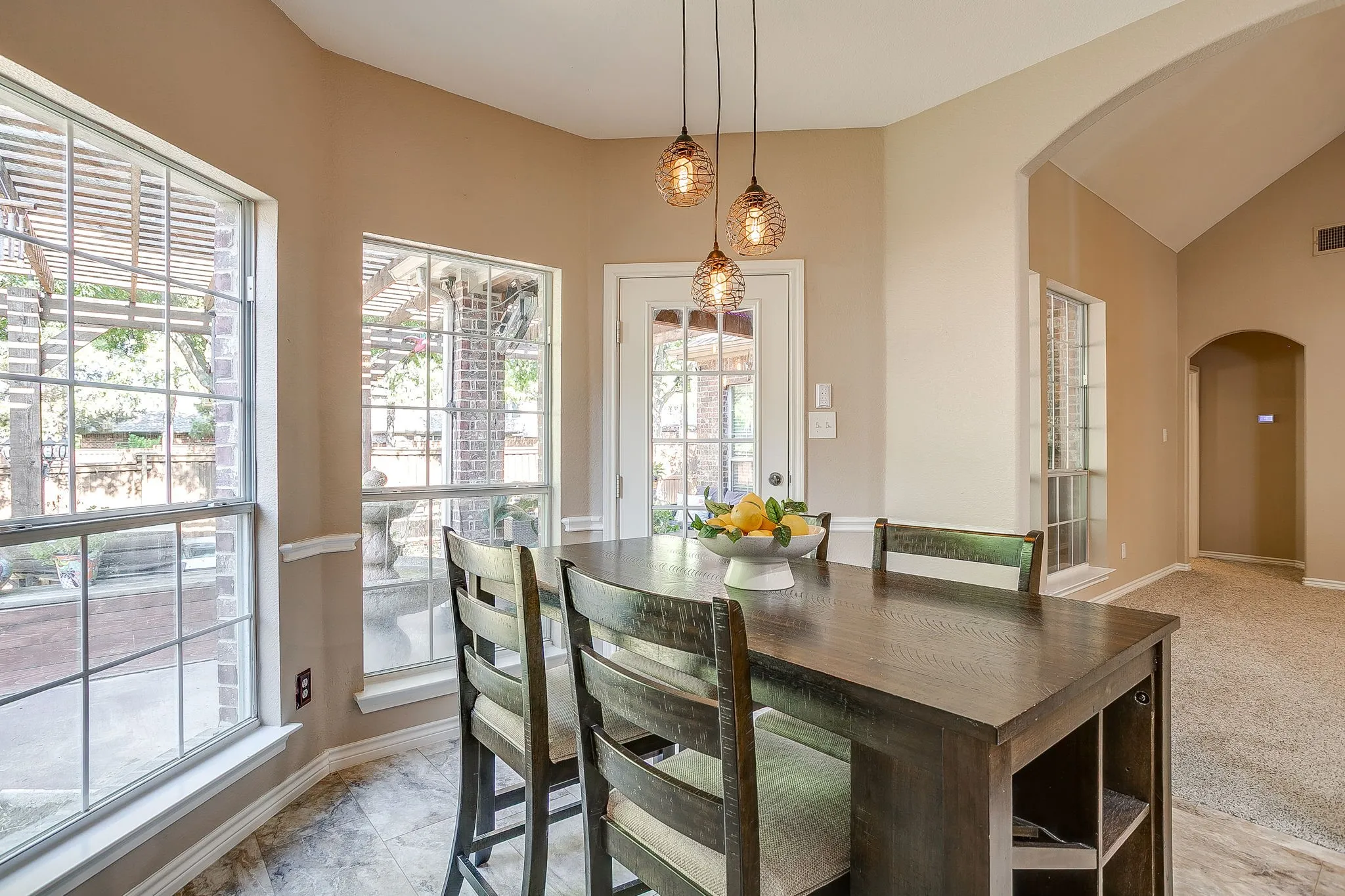 Bay window with multiple panes, three pendant lights, a door with glass panes, and tile flooring