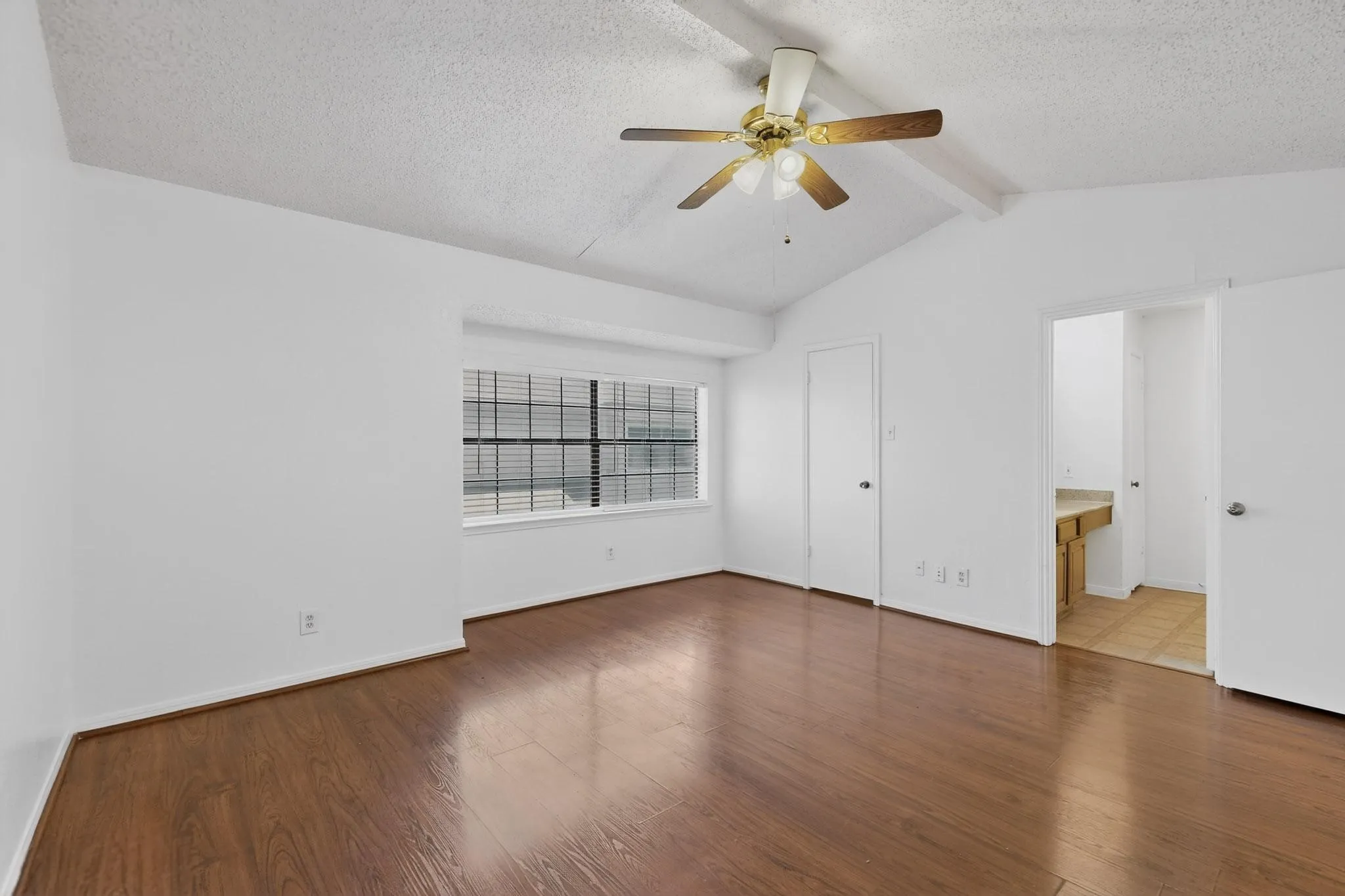 Unfurnished bedroom with a textured ceiling, dark wood-style flooring, beam ceiling, a ceiling fan, and connected bathroom