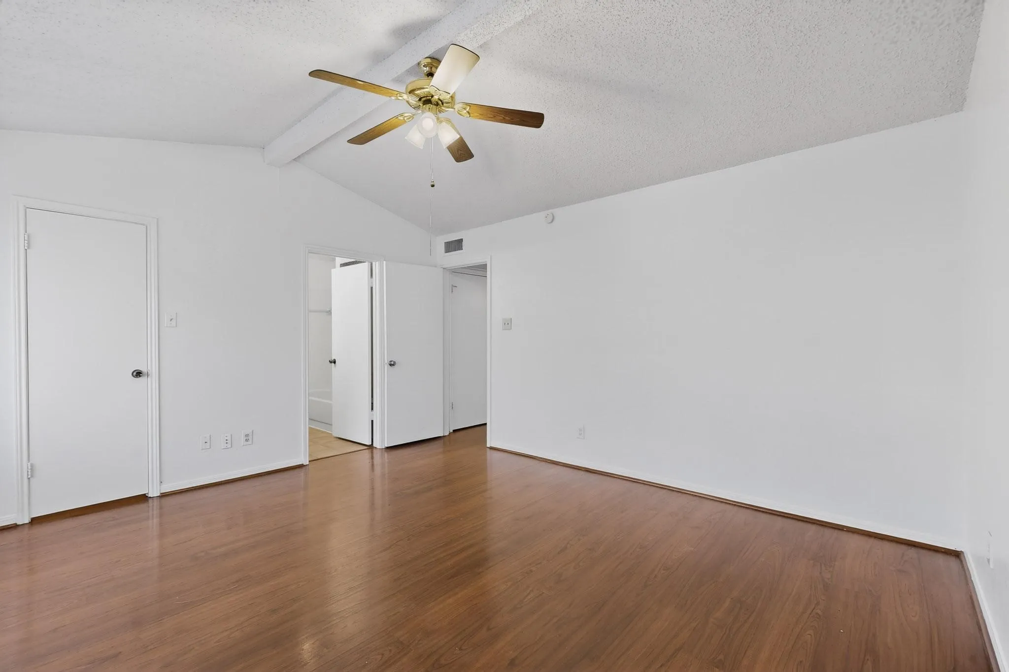 Unfurnished bedroom with beamed ceiling, dark wood-style flooring, a textured ceiling, ceiling fan, and ensuite bath