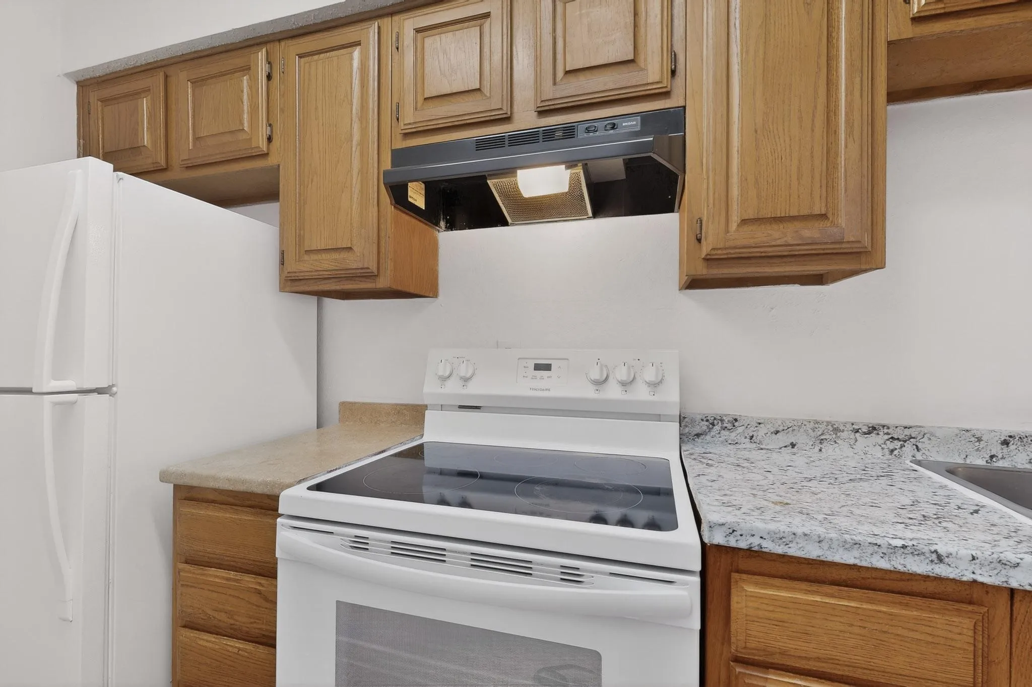 Kitchen featuring white appliances, ventilation hood, light countertops, and wood finish cabinets