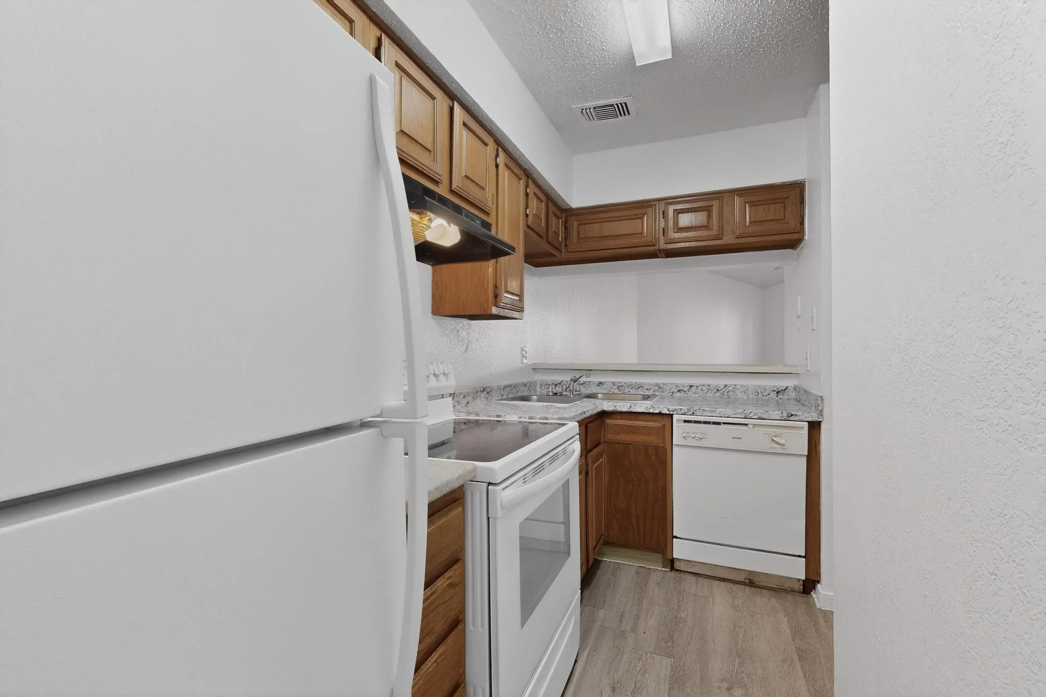 Kitchen with white appliances, light countertops, a textured ceiling, light wood finished floors, and wood finish cabinetry