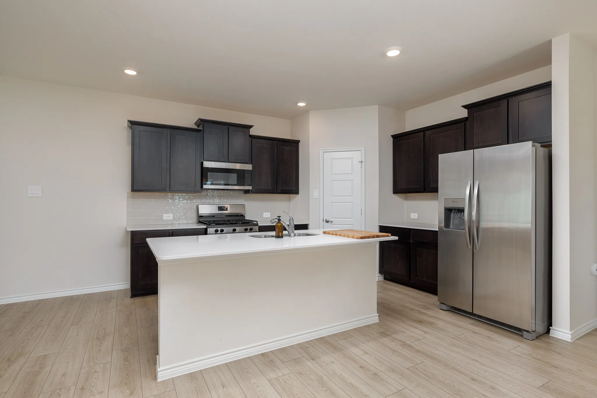 Kitchen featuring wood-finish flooring, dark wood cabinetry, a white countertop island, stainless steel appliances, and recessed lighting