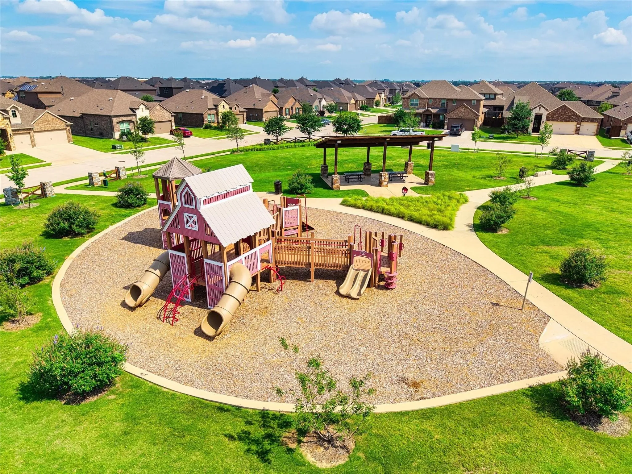 Expansive community green space featuring a playground with slides, a covered picnic area with seating, and paved walking paths