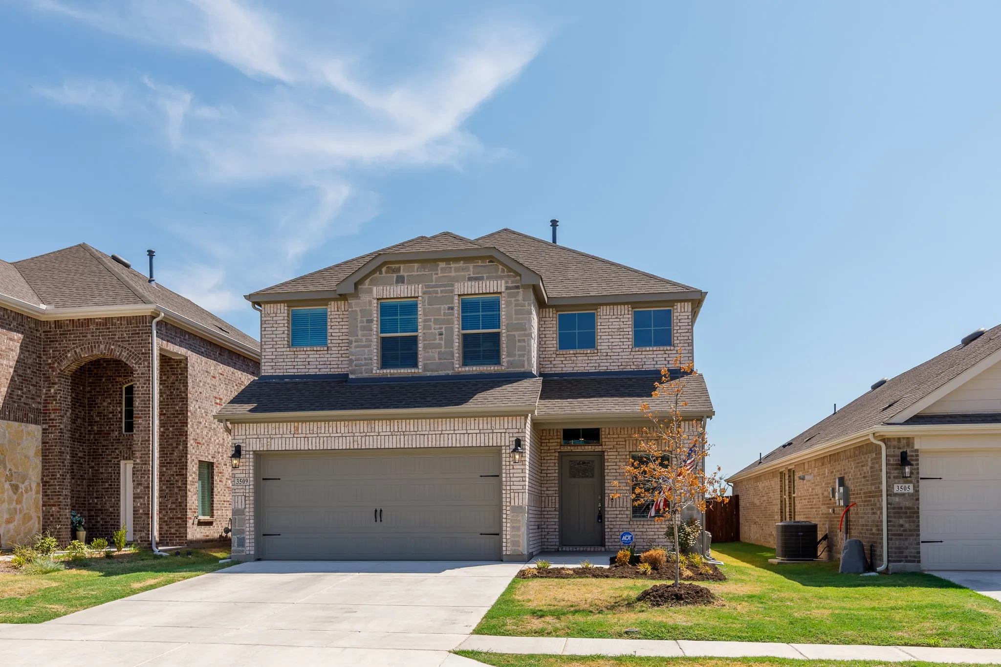 Two-story facade with light brick and stone accents, an attached two-car garage, concrete driveway, and a covered entry