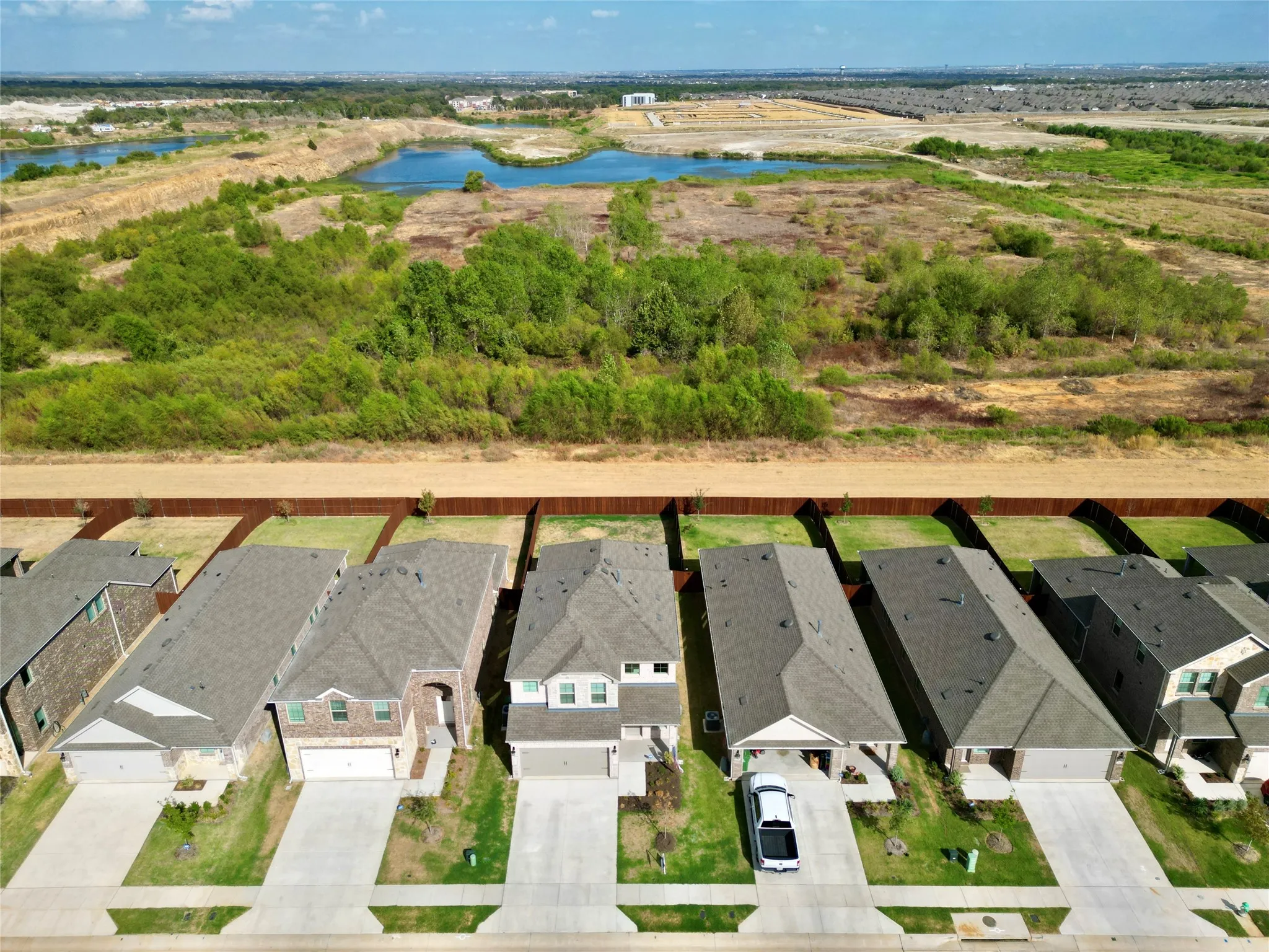 Residential street with concrete driveways, fenced backyards, and expansive natural landscape beyond