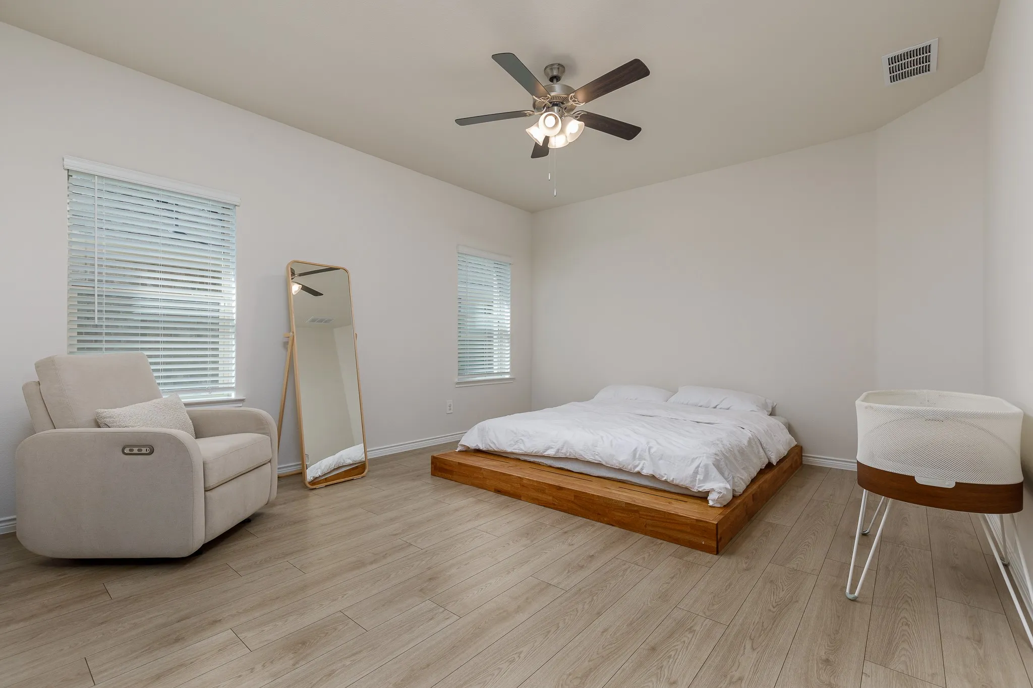 Neutral wall paint with wood-finish flooring, two windows with blinds, and a ceiling fan with integrated lighting