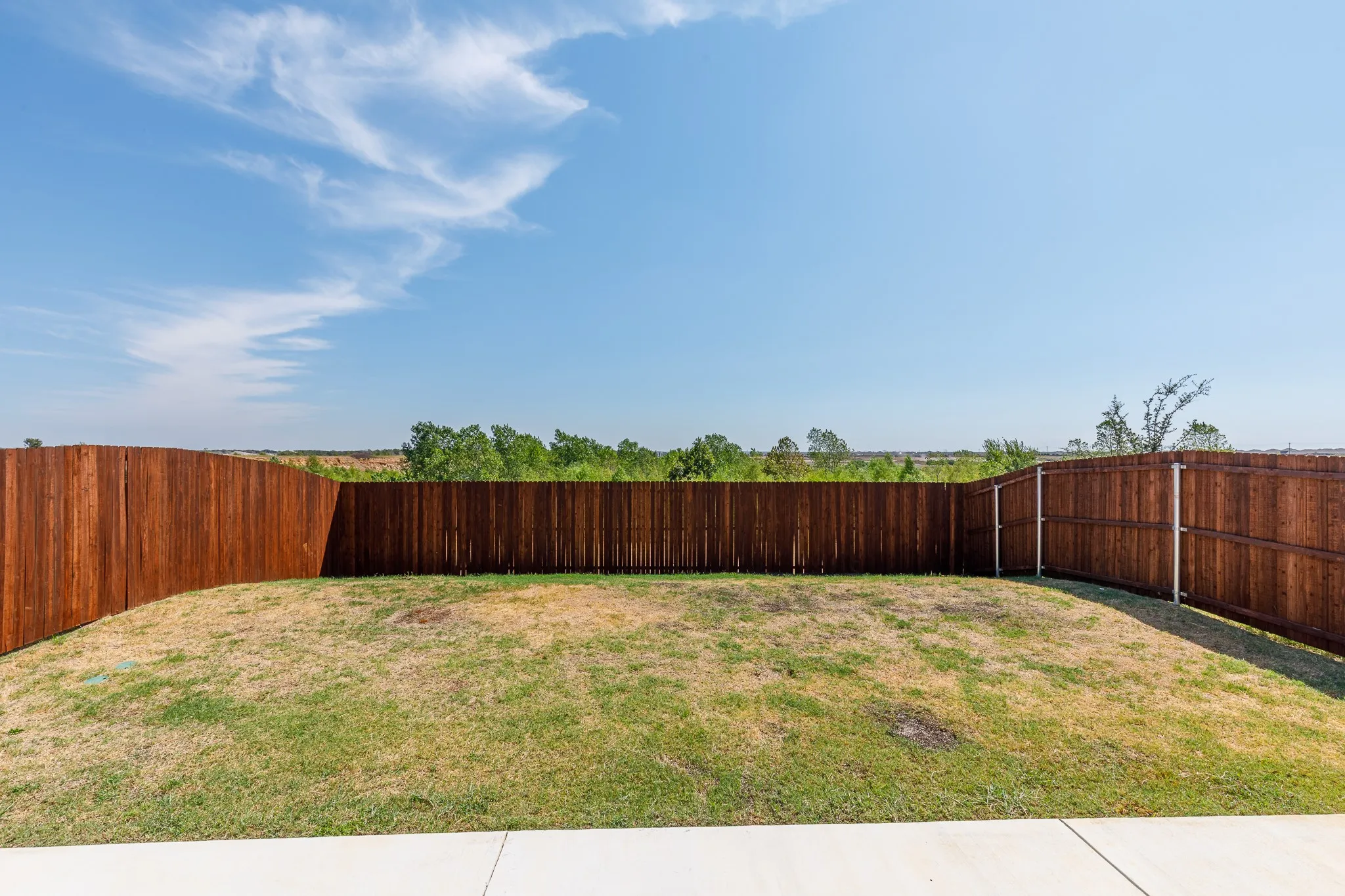 Expansive fenced yard featuring a concrete patio, wood privacy fencing, and green space