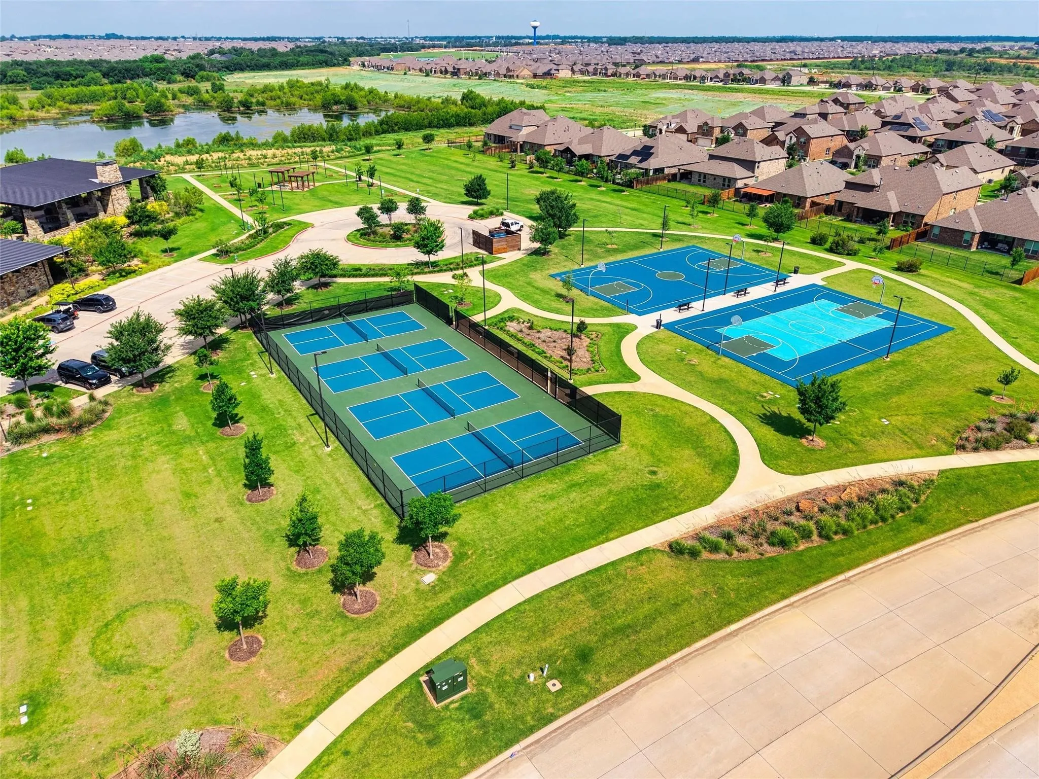 Multiple pickleball courts, two basketball courts, a manicured green space, and a pond with surrounding greenery