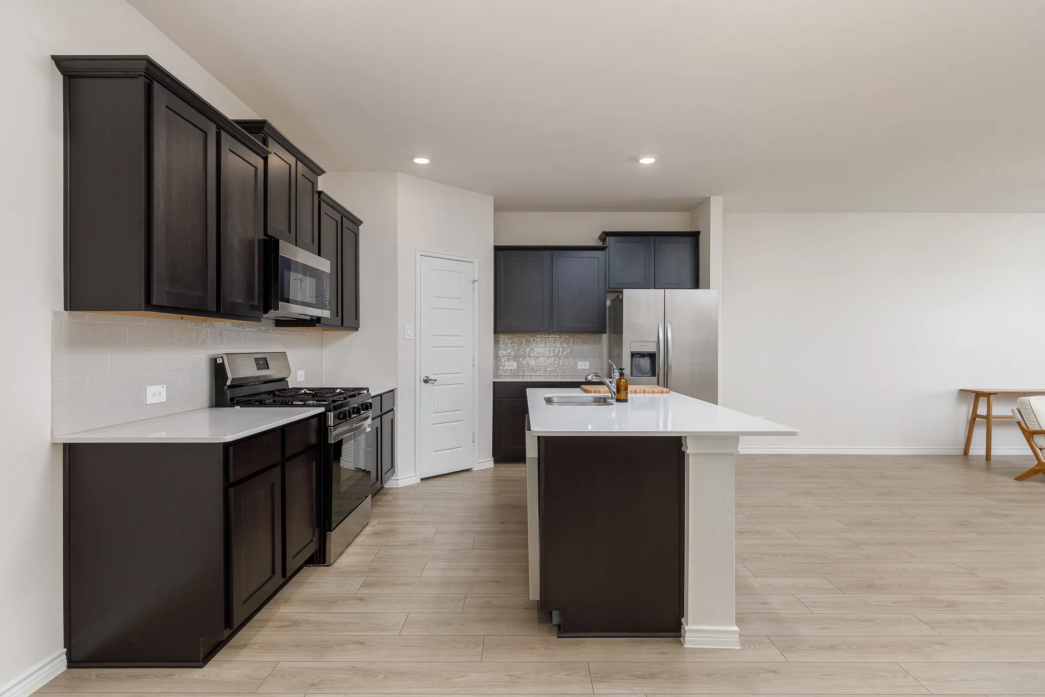Kitchen featuring dark wood cabinetry, stainless steel appliances, a white tile backsplash, and a large central island with a white countertop
