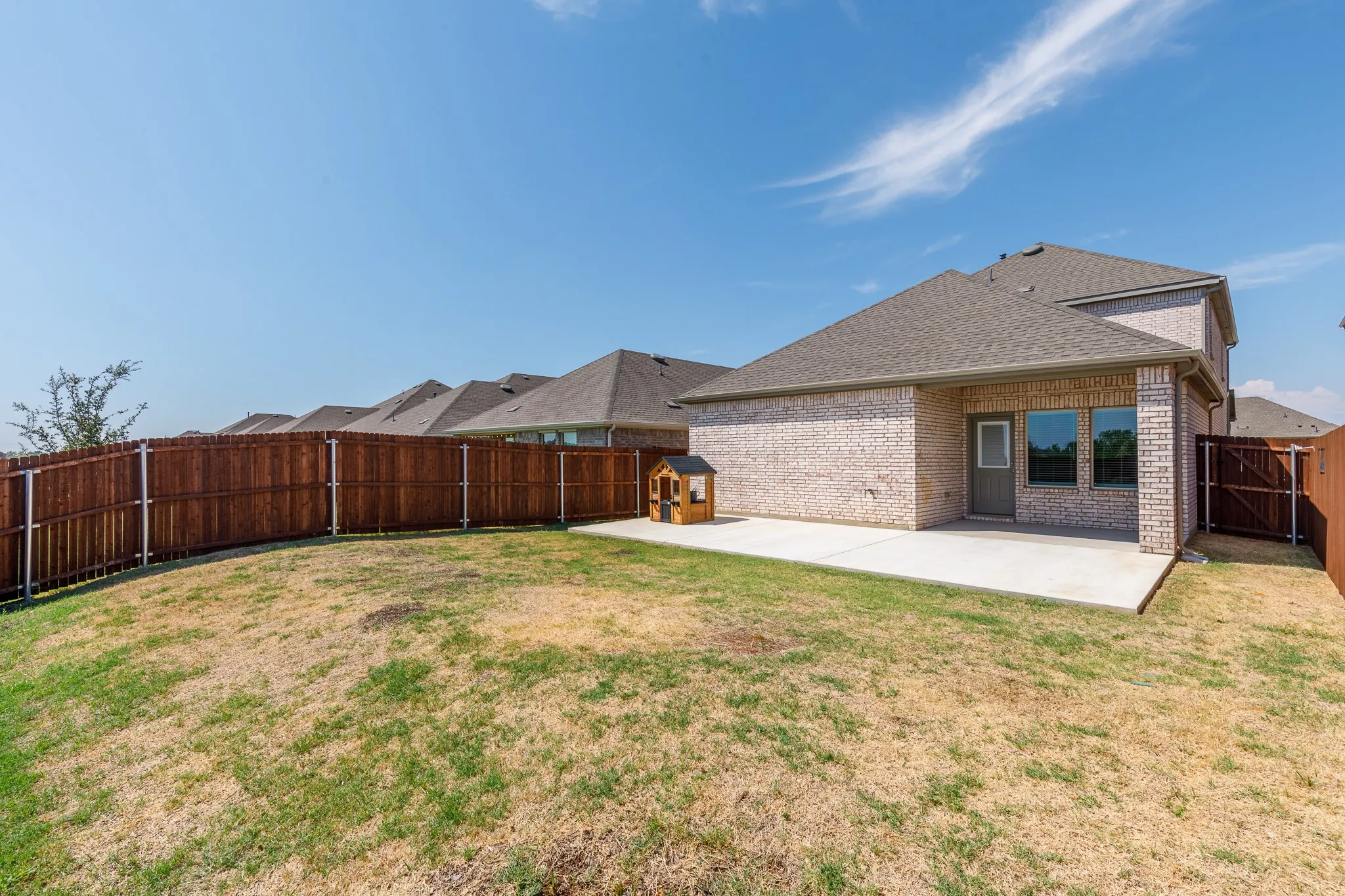 Expansive backyard with a wood privacy fence, concrete patio, and brick exterior
