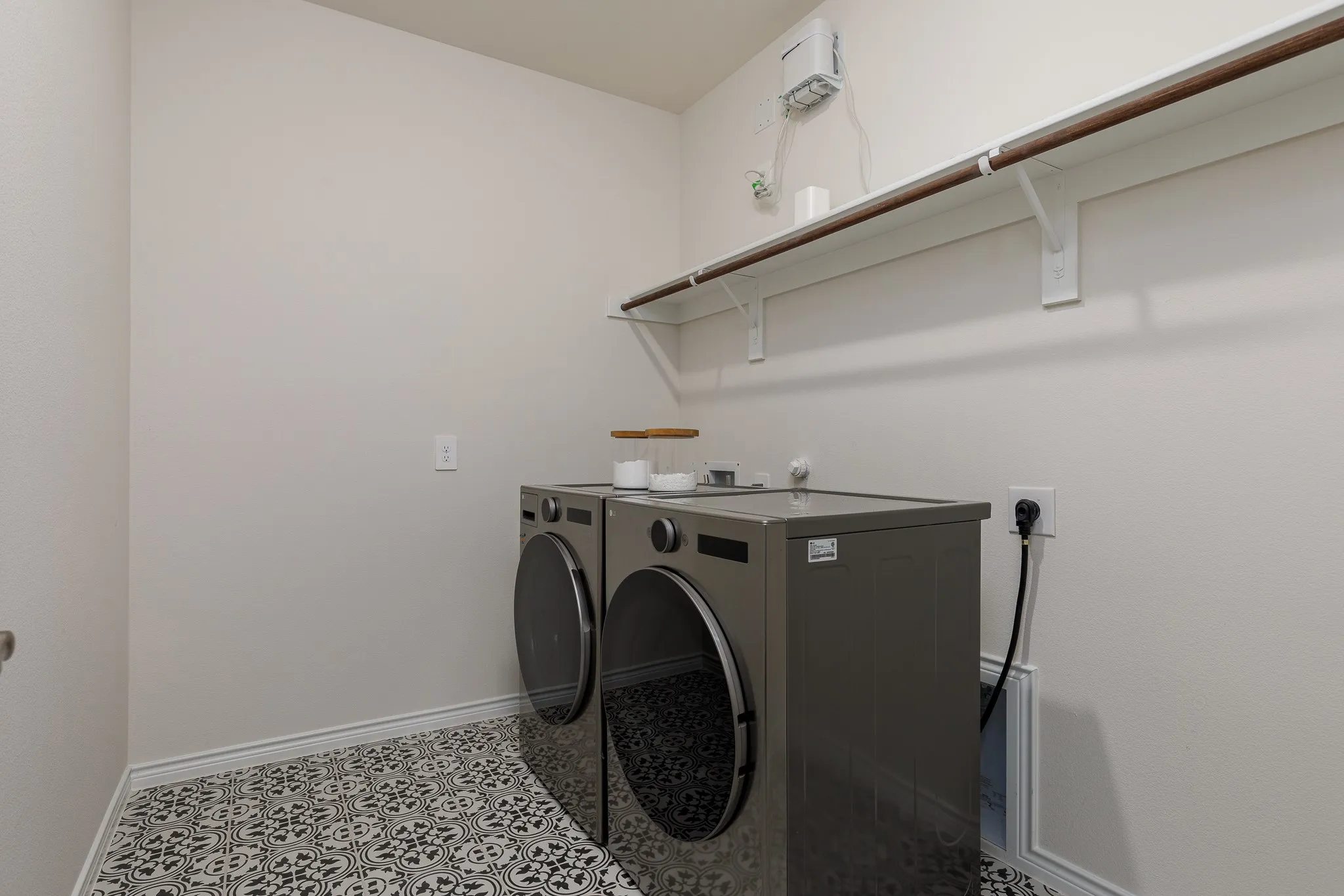 Integrated laundry area featuring patterned floor tile, overhead shelving, and a hanging rod