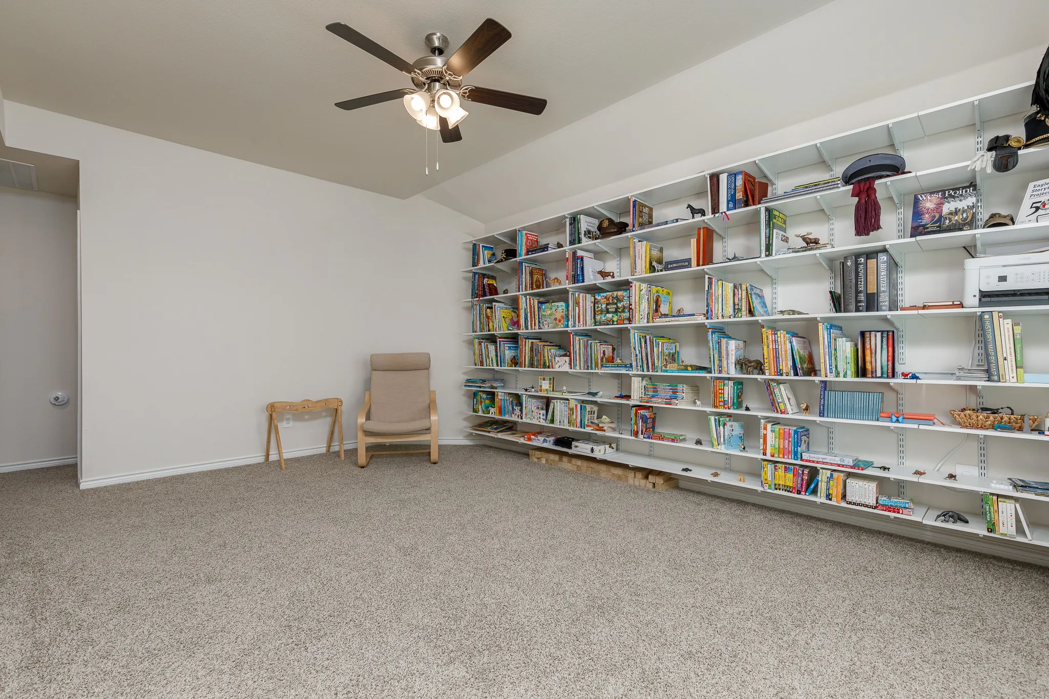 Expansive wall-mounted shelving unit, neutral-toned carpeting, and a ceiling fan with integrated lighting