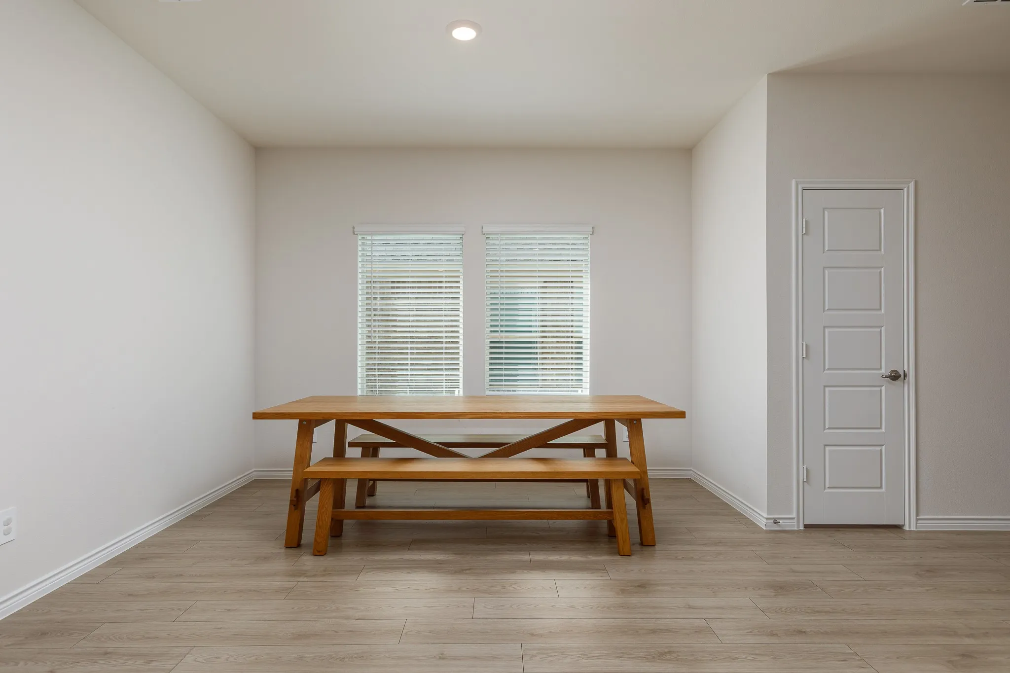 Recessed lighting, wood-finish flooring, two windows with blinds, and a paneled door with a spherical knob