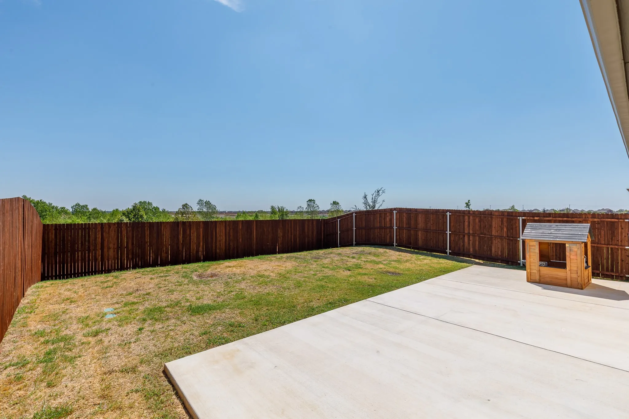 Expansive backyard featuring a privacy fence, concrete patio, and a grass lawn