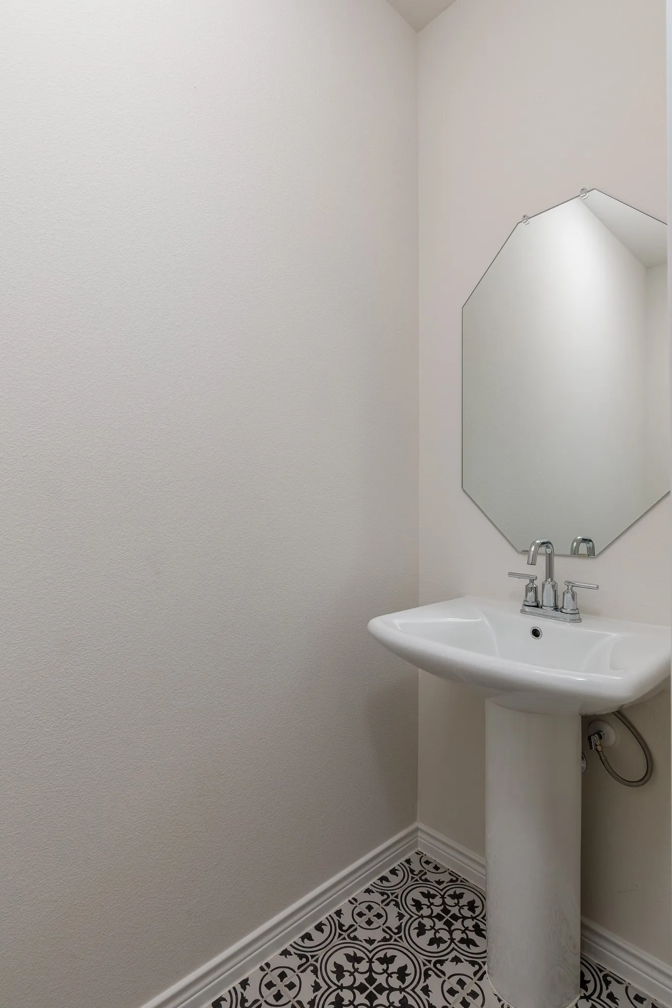 Pedestal sink with chrome fixtures, octagonal wall mirror, and patterned floor tile