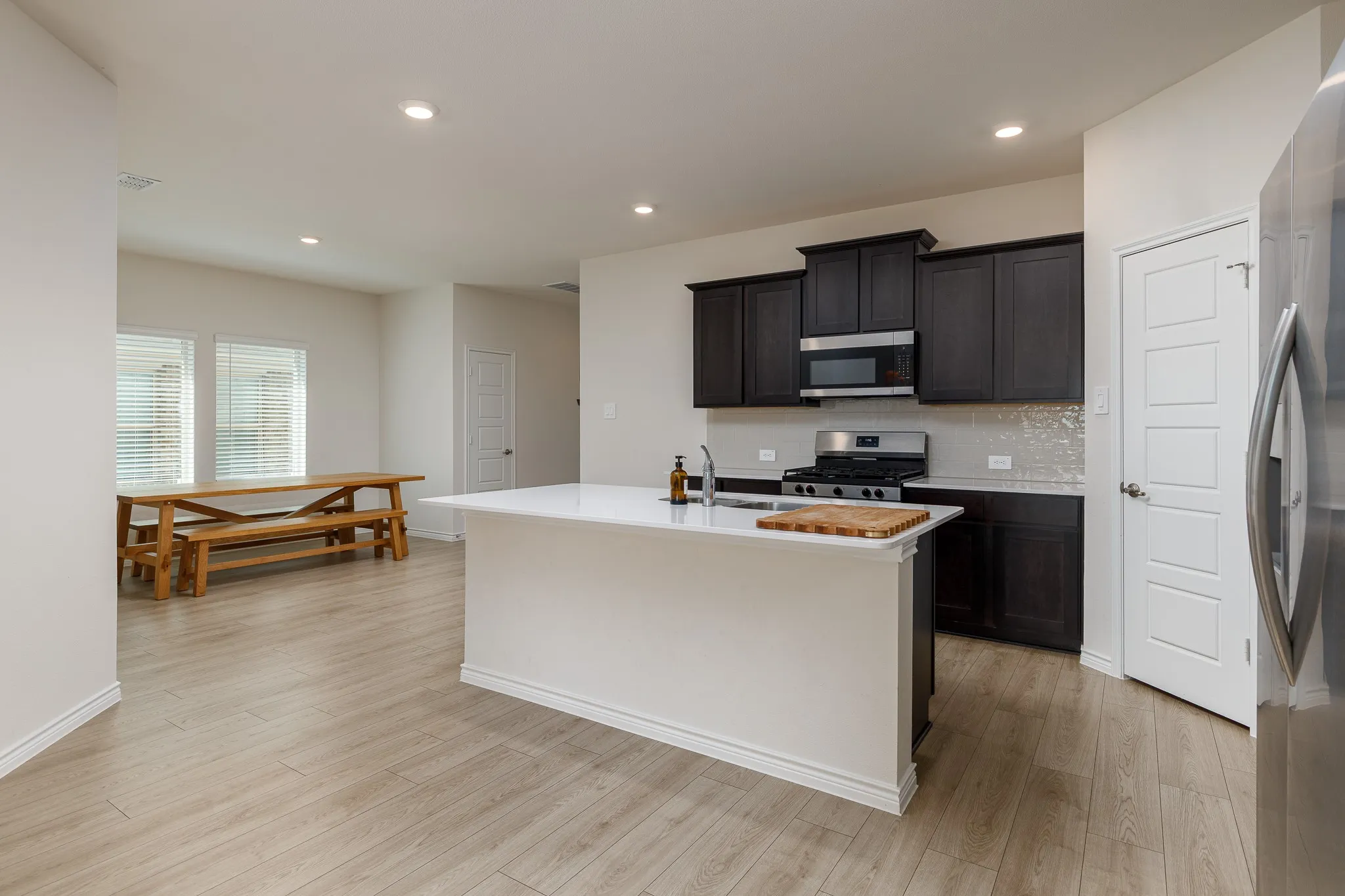 Kitchen island with white countertop, dark wood-finish cabinetry, stainless steel appliances, and tile backsplash