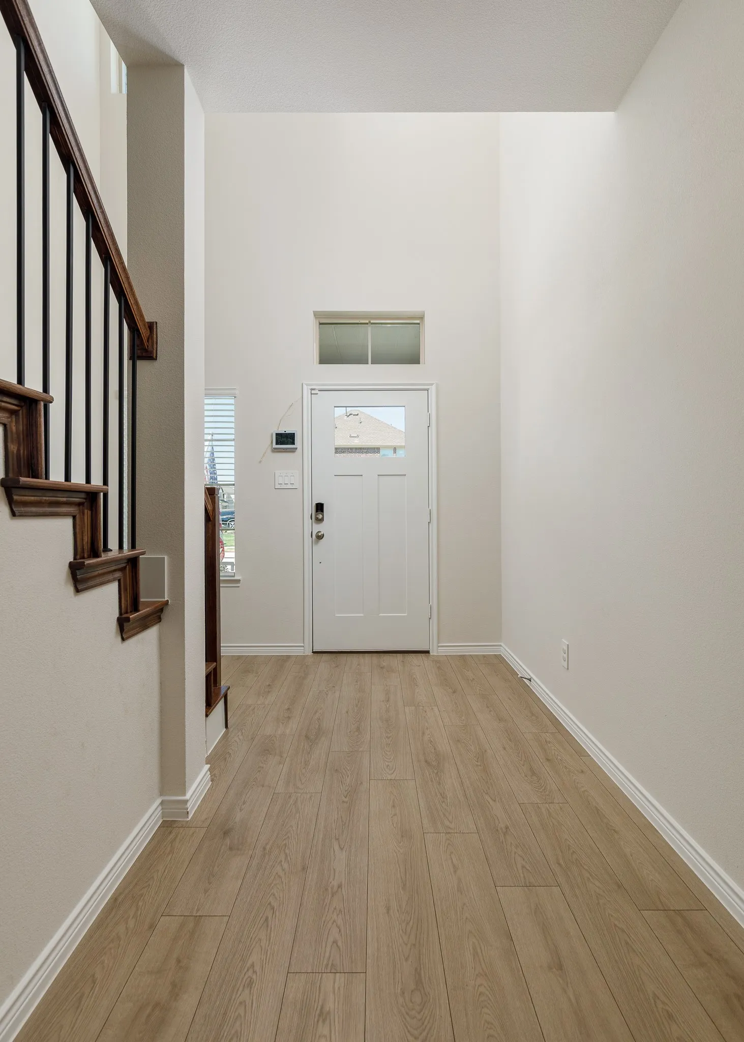 Entryway featuring wood-finish flooring, a white paneled door with a transom window, and a staircase with wood handrails and black metal balusters
