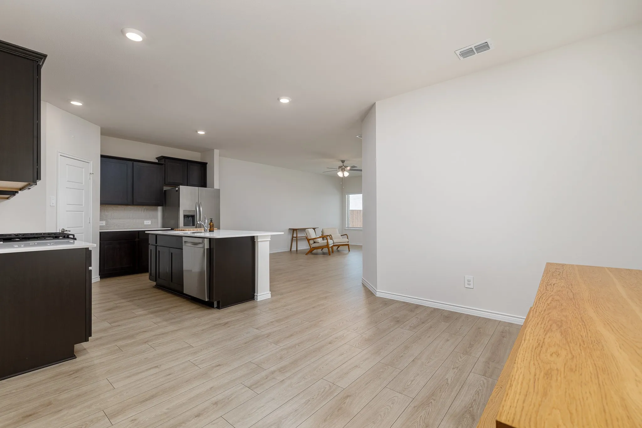 Kitchen featuring dark wood cabinetry, a center island with a white countertop, stainless steel appliances, and wood-finish flooring extending into the open concept space