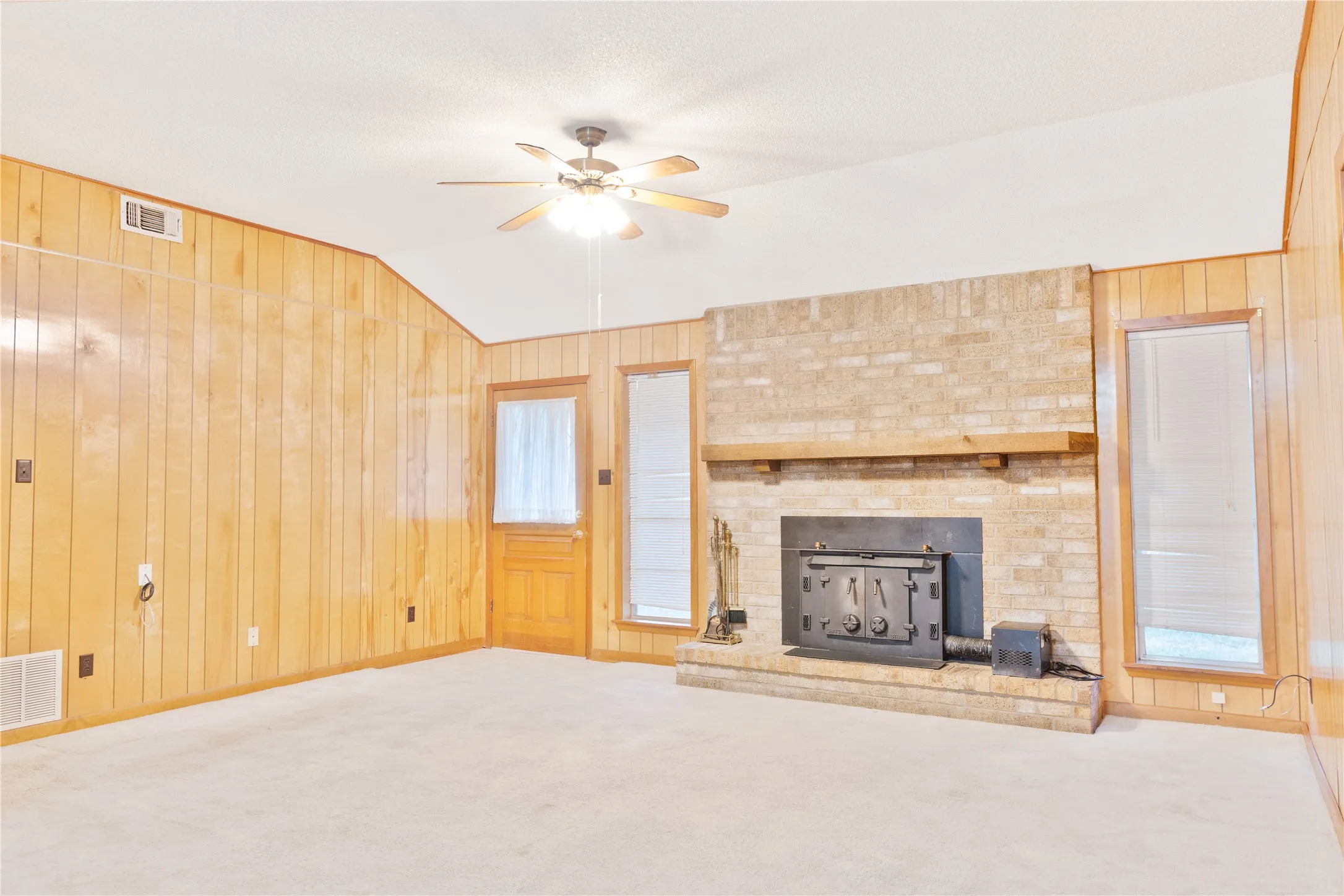 Brick fireplace with a wood mantle, wood paneling, and ceiling fan