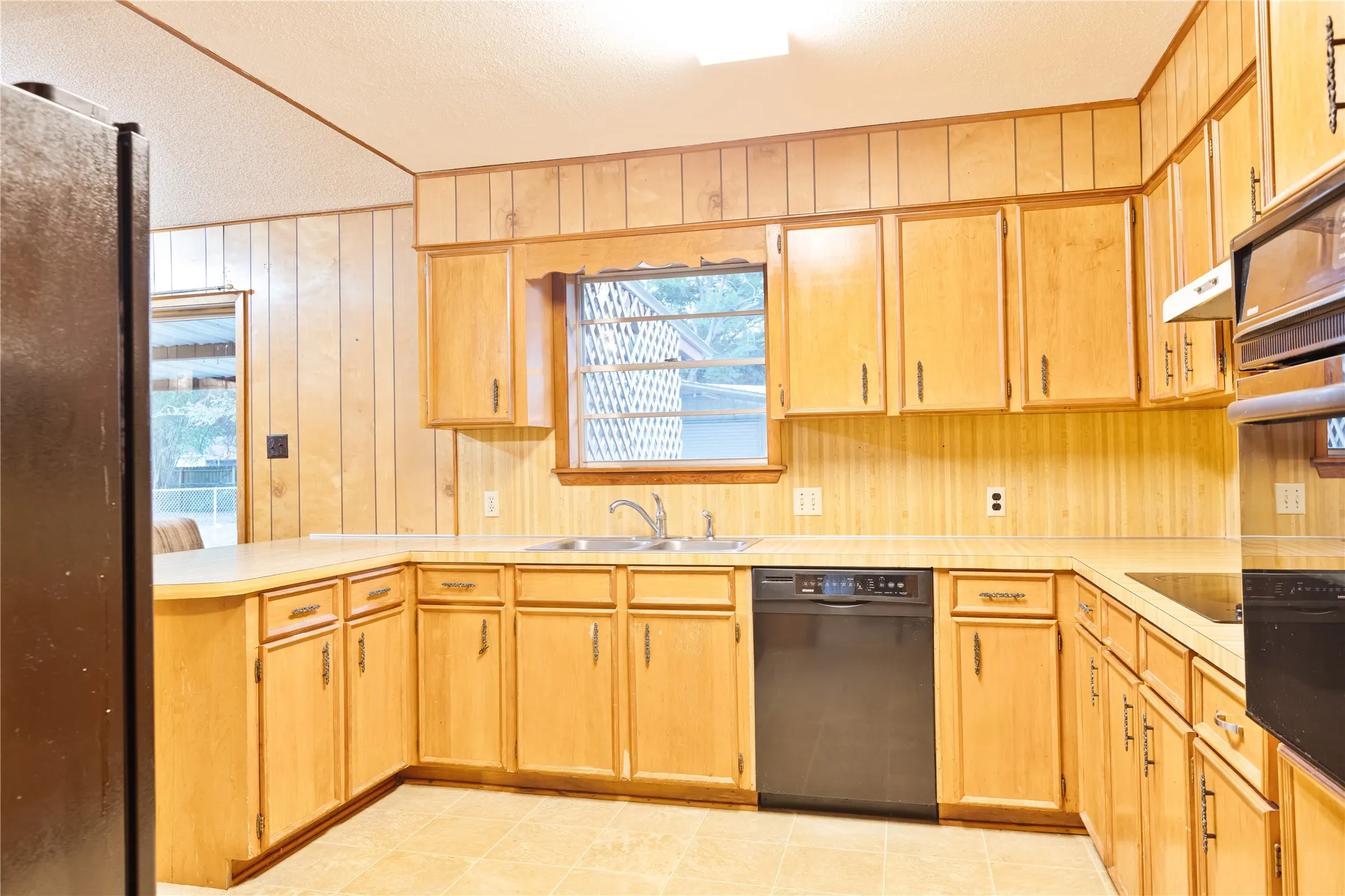 Kitchen featuring wood-finish cabinetry, built-in black appliances, a double basin sink, and laminate countertops