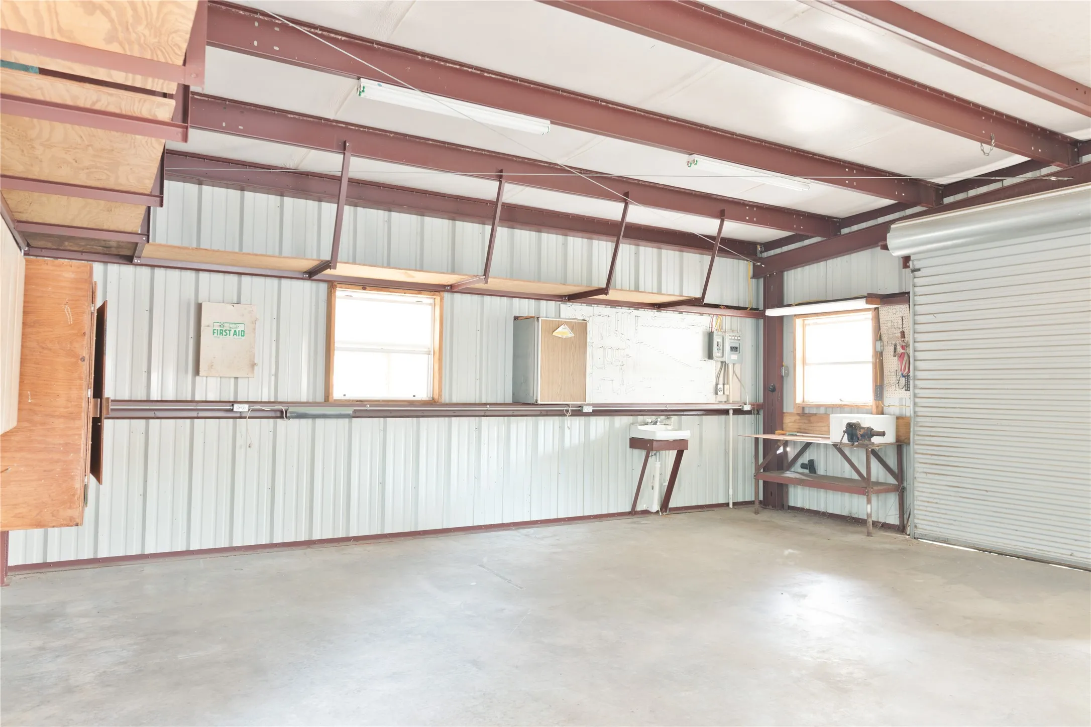 Concrete flooring, exposed structural beams, high ceilings, multiple windows, and a roll-up door