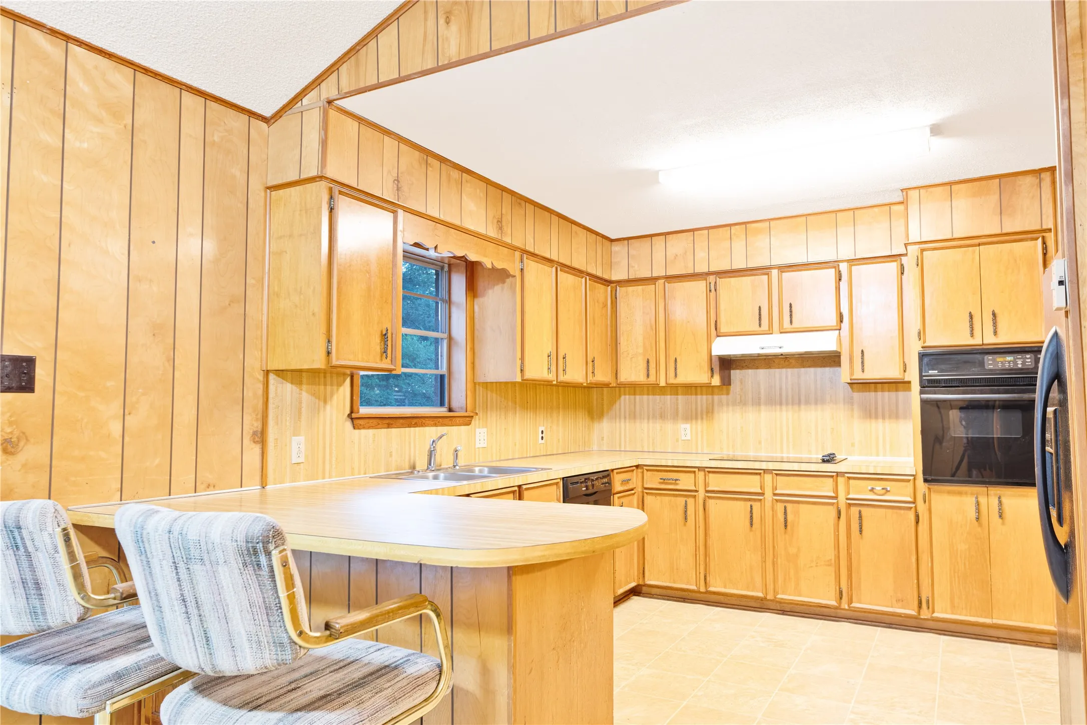 Kitchen featuring extensive wood paneling, wood-finish cabinetry, built-in oven, and a built-in cooktop