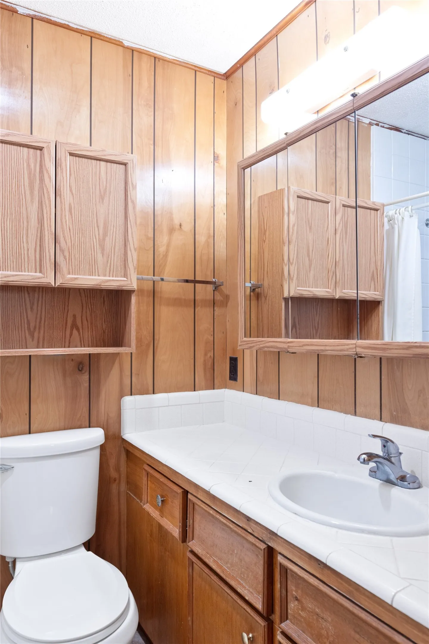 Wood paneling throughout, white tiled countertop, wood-finish vanity, recessed mirrored medicine cabinet, and built-in wood-finish cabinetry