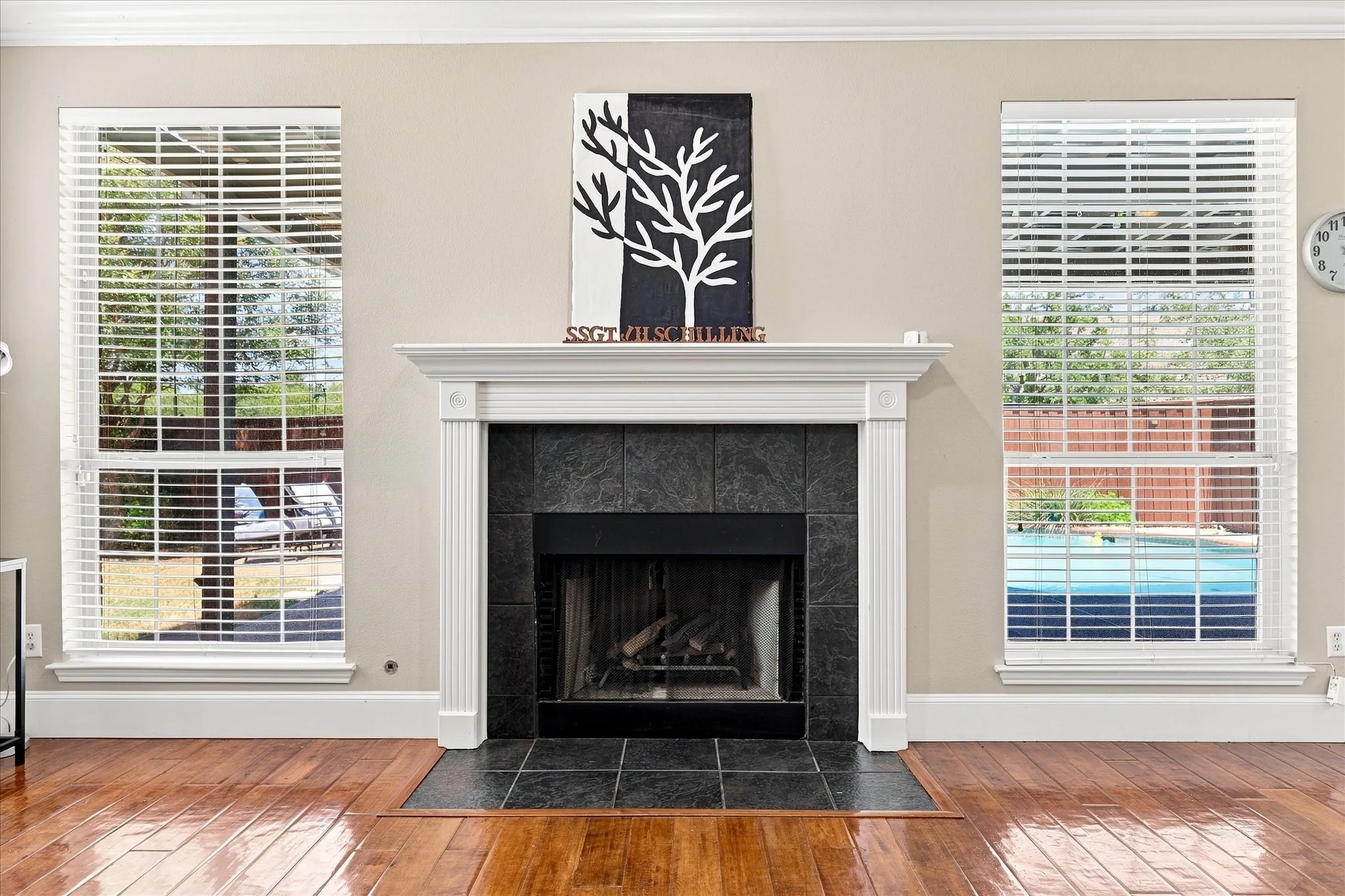 Fireplace with a white mantle and a dark tile surround, dark tile hearth, wood-finish flooring, dual windows with white blinds, and crown molding