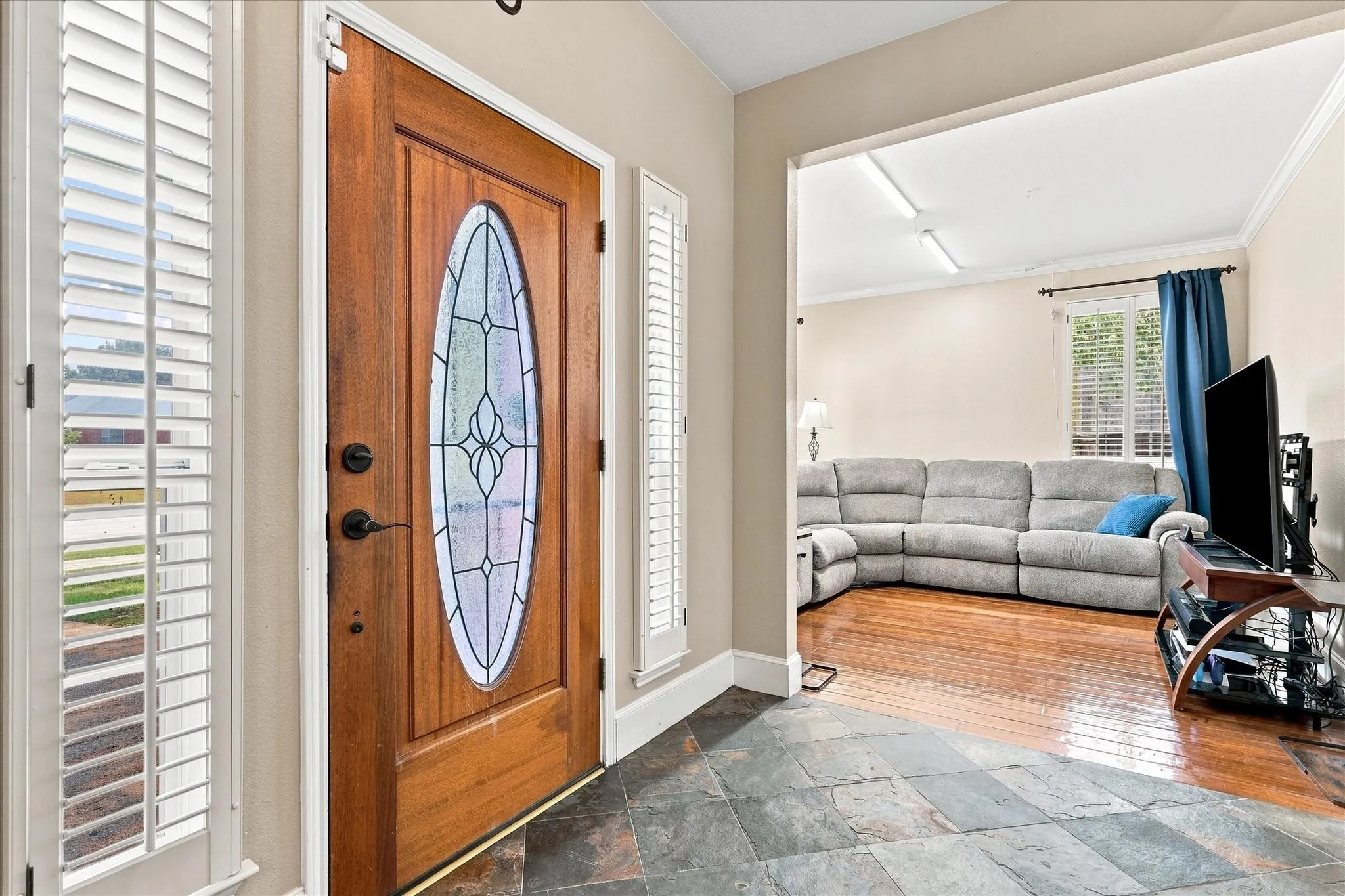 Entryway featuring a wood-finish door with an oval stained-glass insert, slate tile flooring, and white plantation shutters