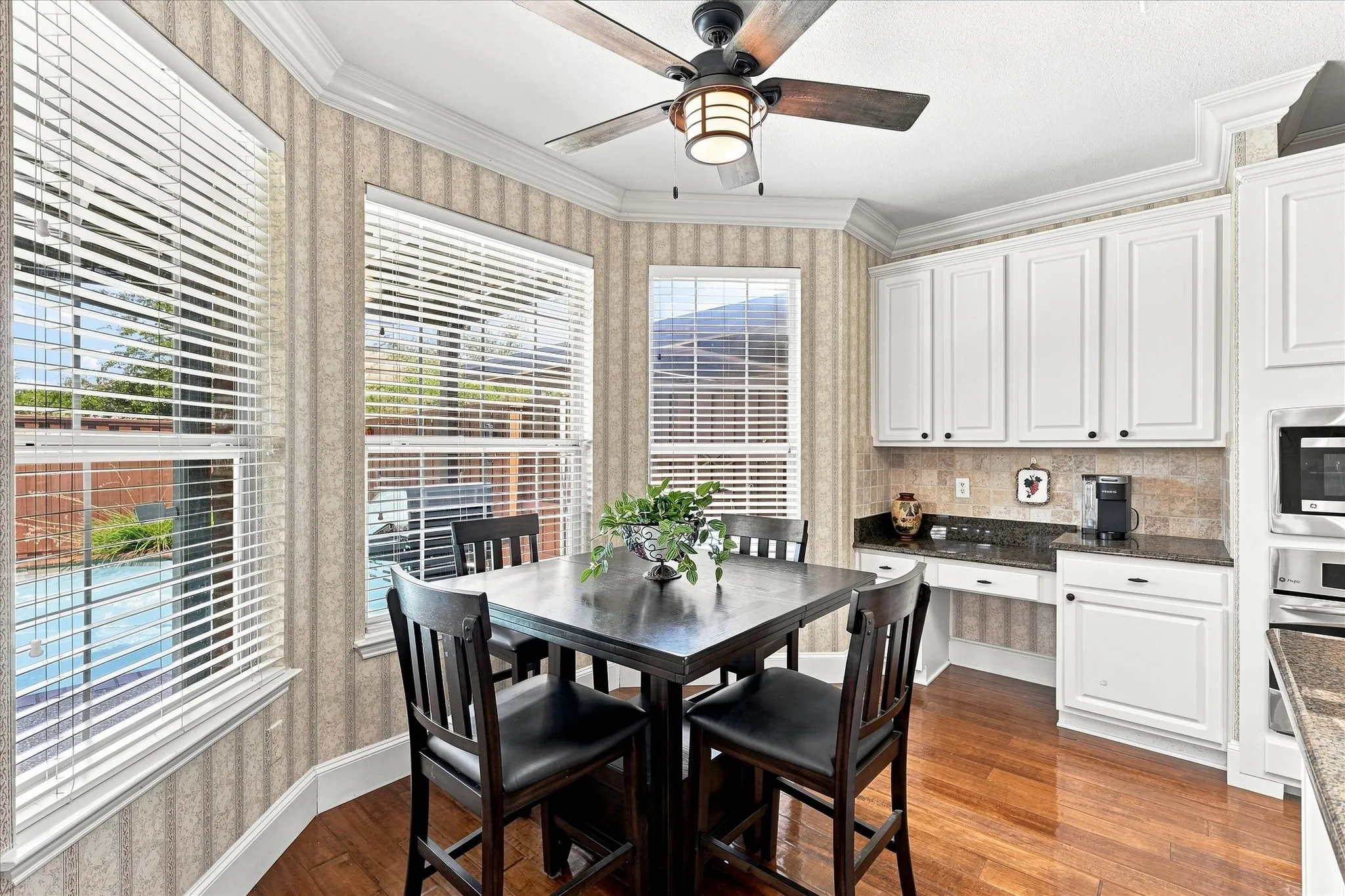 Bay window with natural light, wood-finish flooring, built-in cabinetry, stone countertops, and a ceiling fan