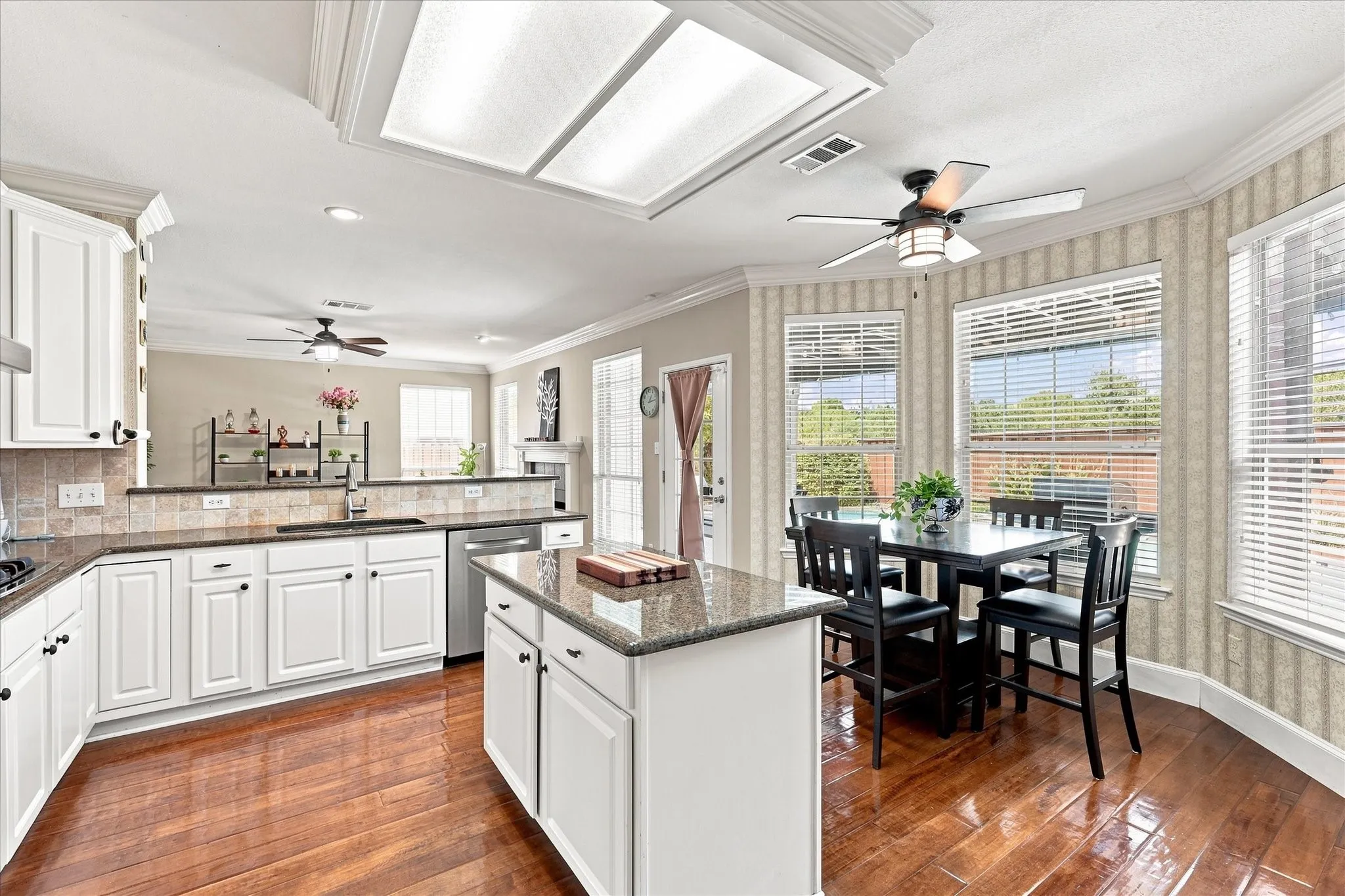 Kitchen featuring wood-finish flooring, white cabinetry, a central island with a stone countertop, and a built-in dishwasher